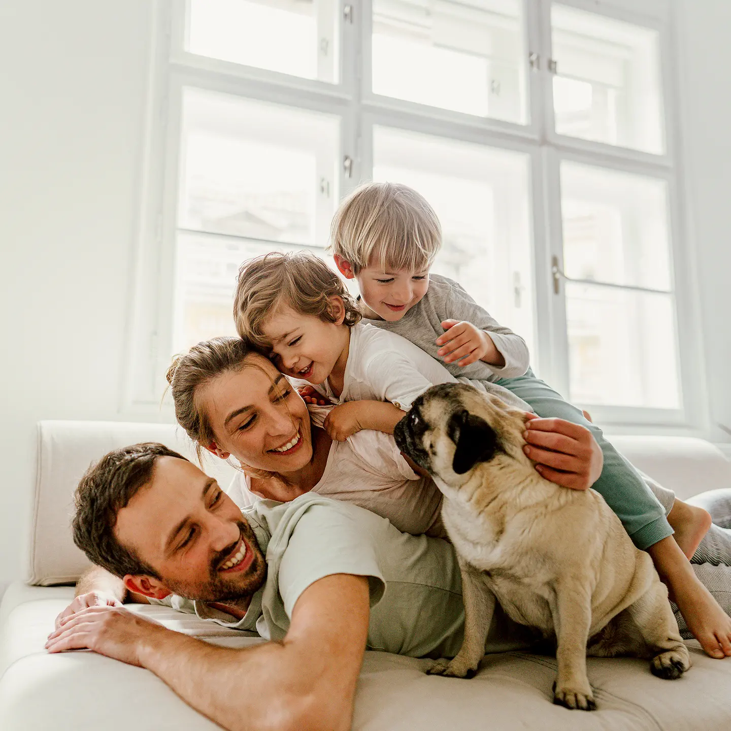 Eine Familie liegt mit zwei Kindern und einem Hund auf einer weißen Couch.