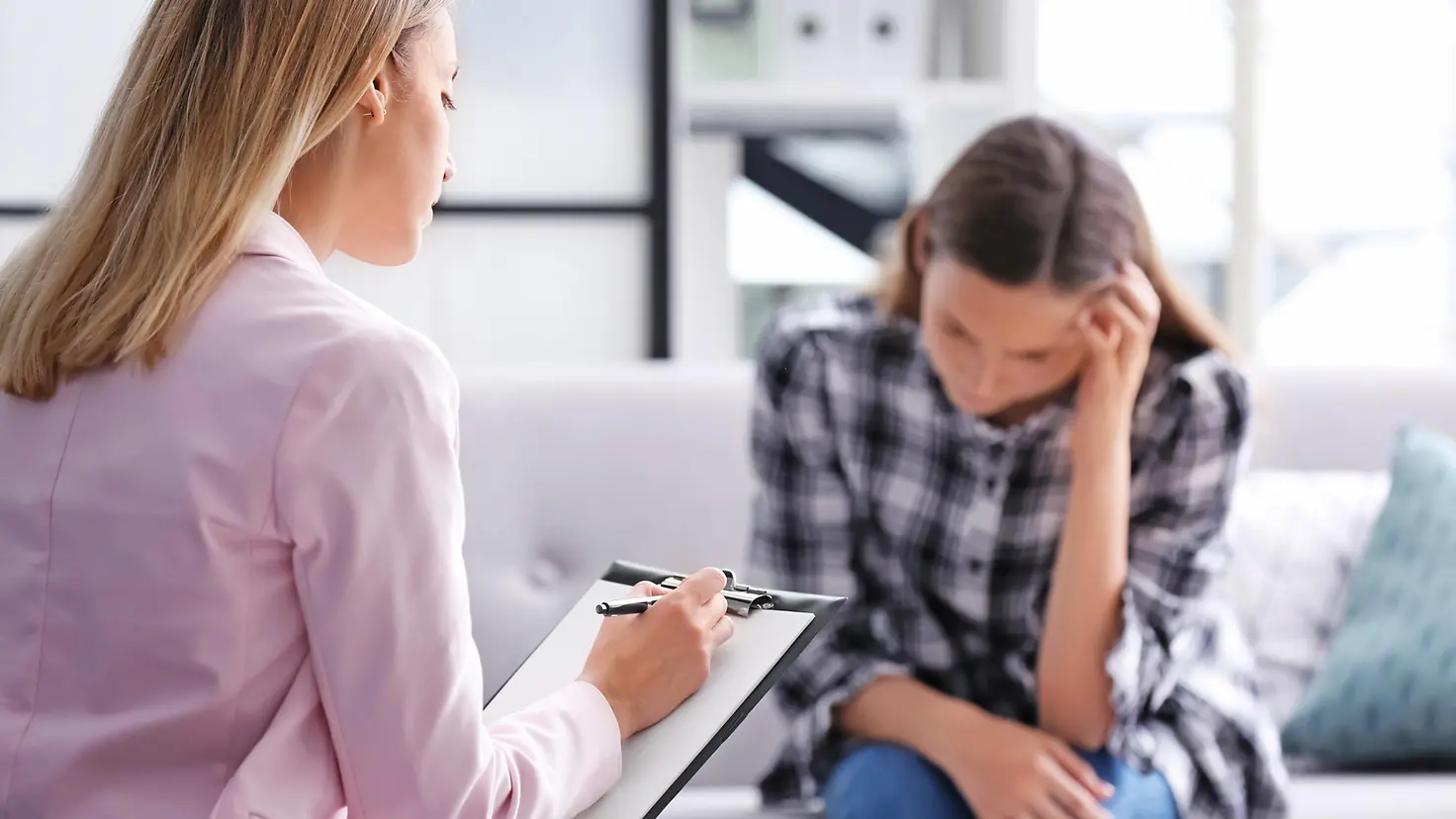 Eine Psychotherapeutin macht sich Notizen zur jungen Frau, die ihr gegenüber sitzt.