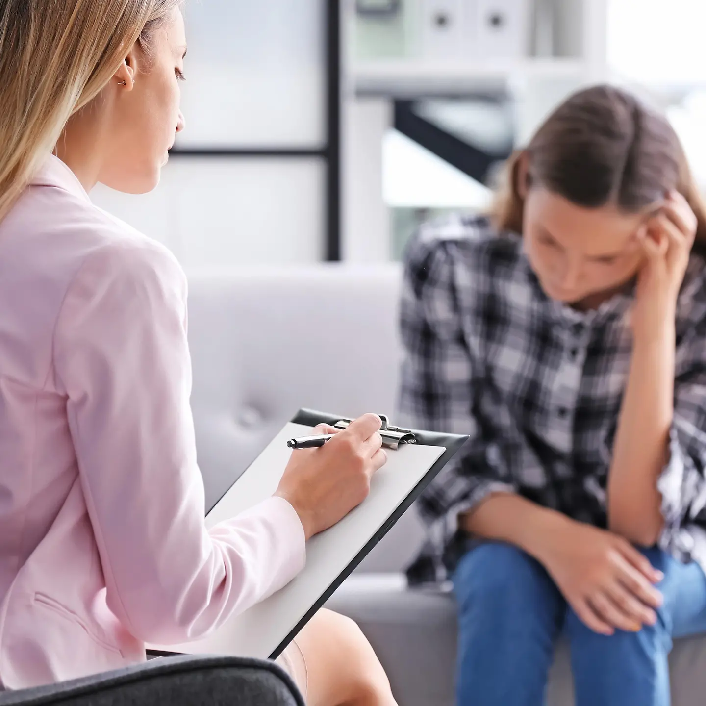 Eine Psychotherapeutin macht sich Notizen zur jungen Frau, die ihr gegenüber sitzt.