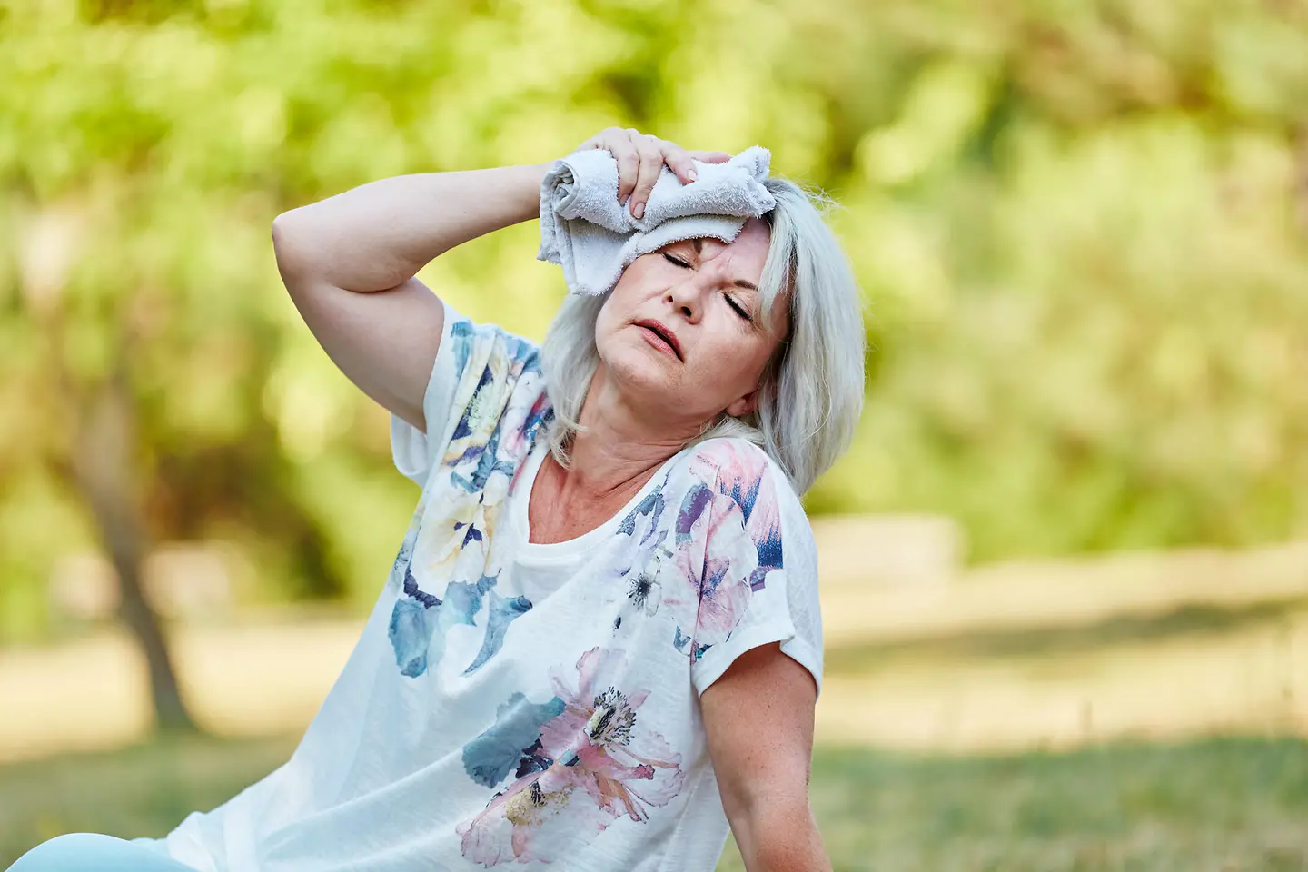 Das Bild zeigt eine Frau, die ihren Kopf mit einem kalten Tuch kühlt.