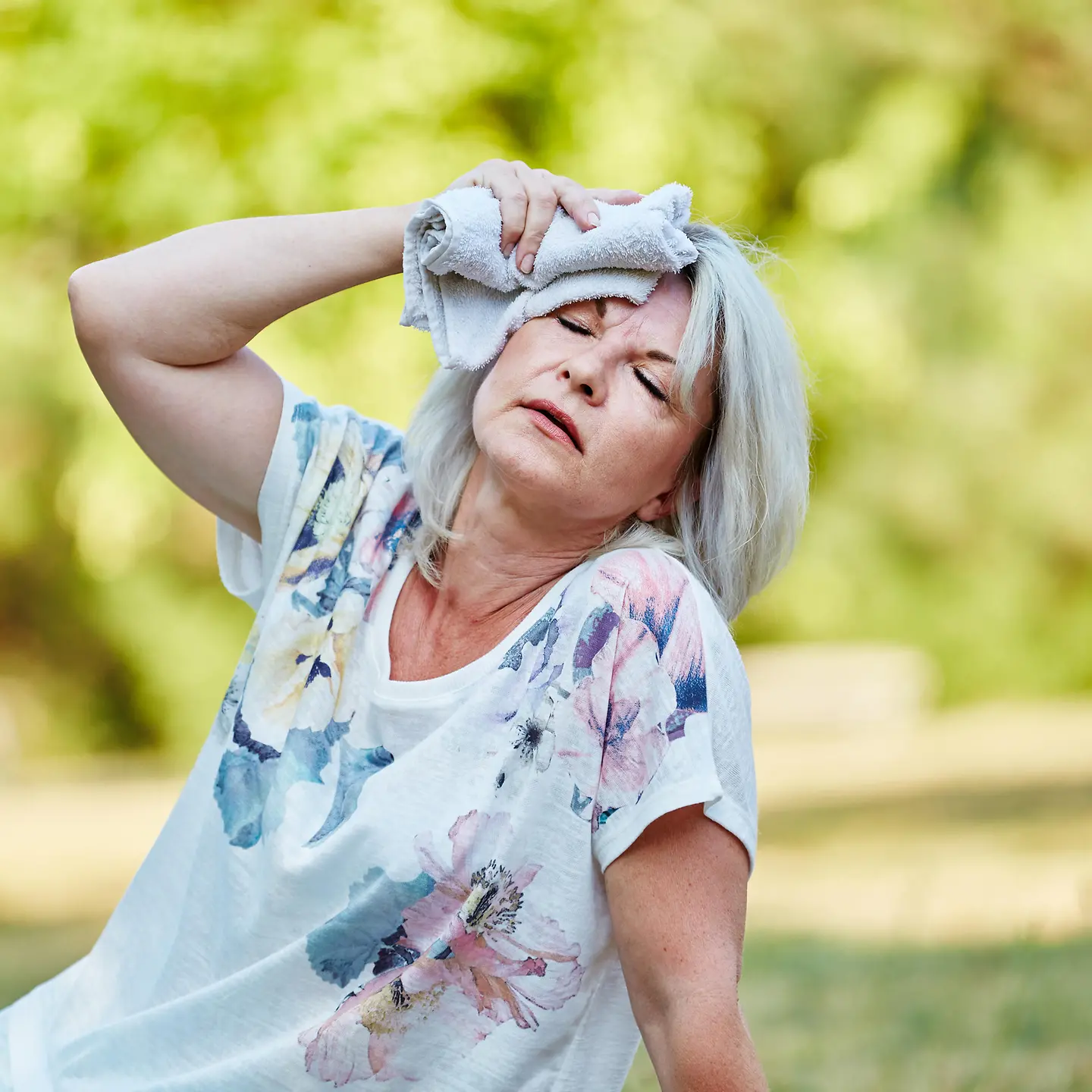 Das Bild zeigt eine Frau, die ihren Kopf mit einem kalten Tuch kühlt.