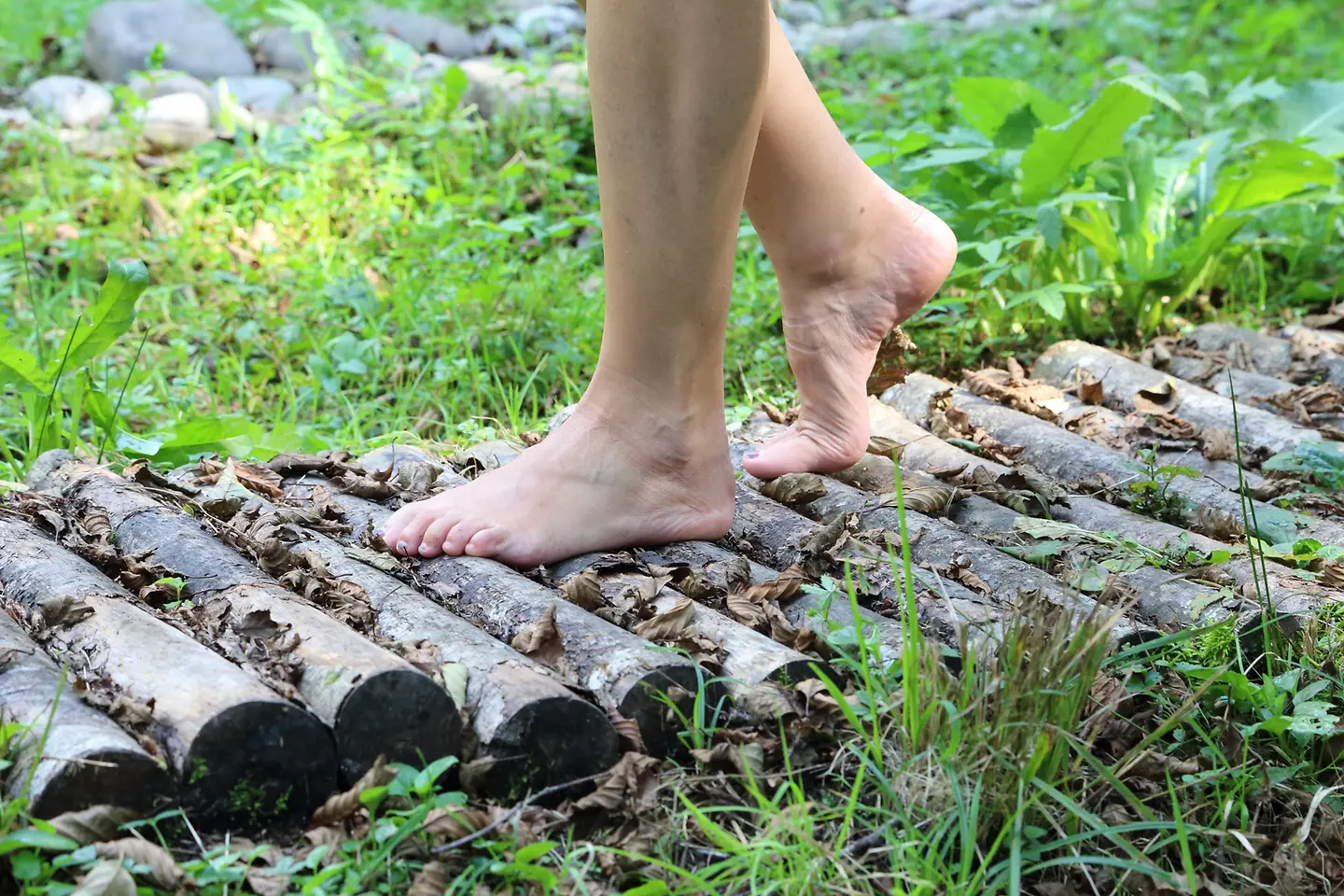 Das Bild zeigt eine Person, die barfuß über einen Weg läuft.