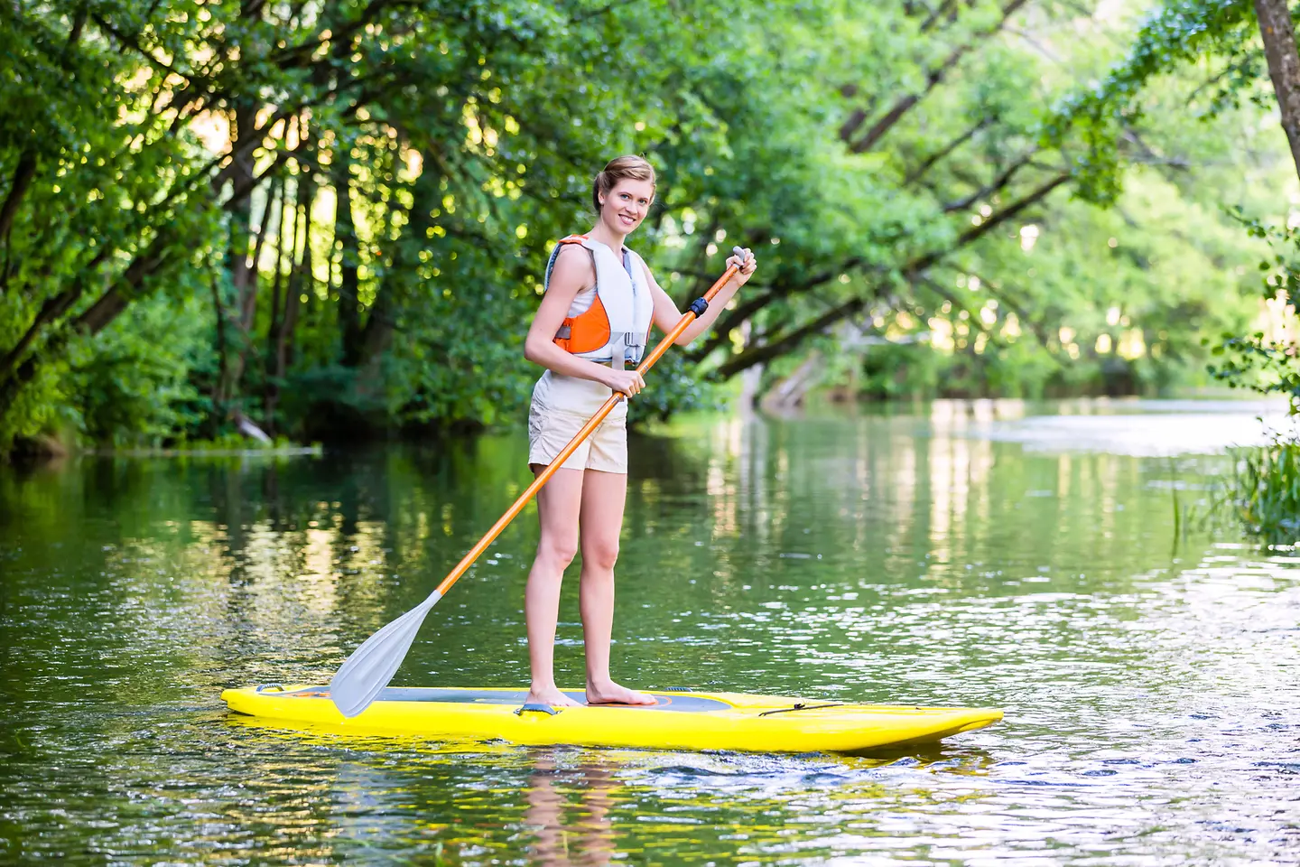 Das Bild zeigt eine Frau, die auf einem See Stand-Up-Paddling betreibt.