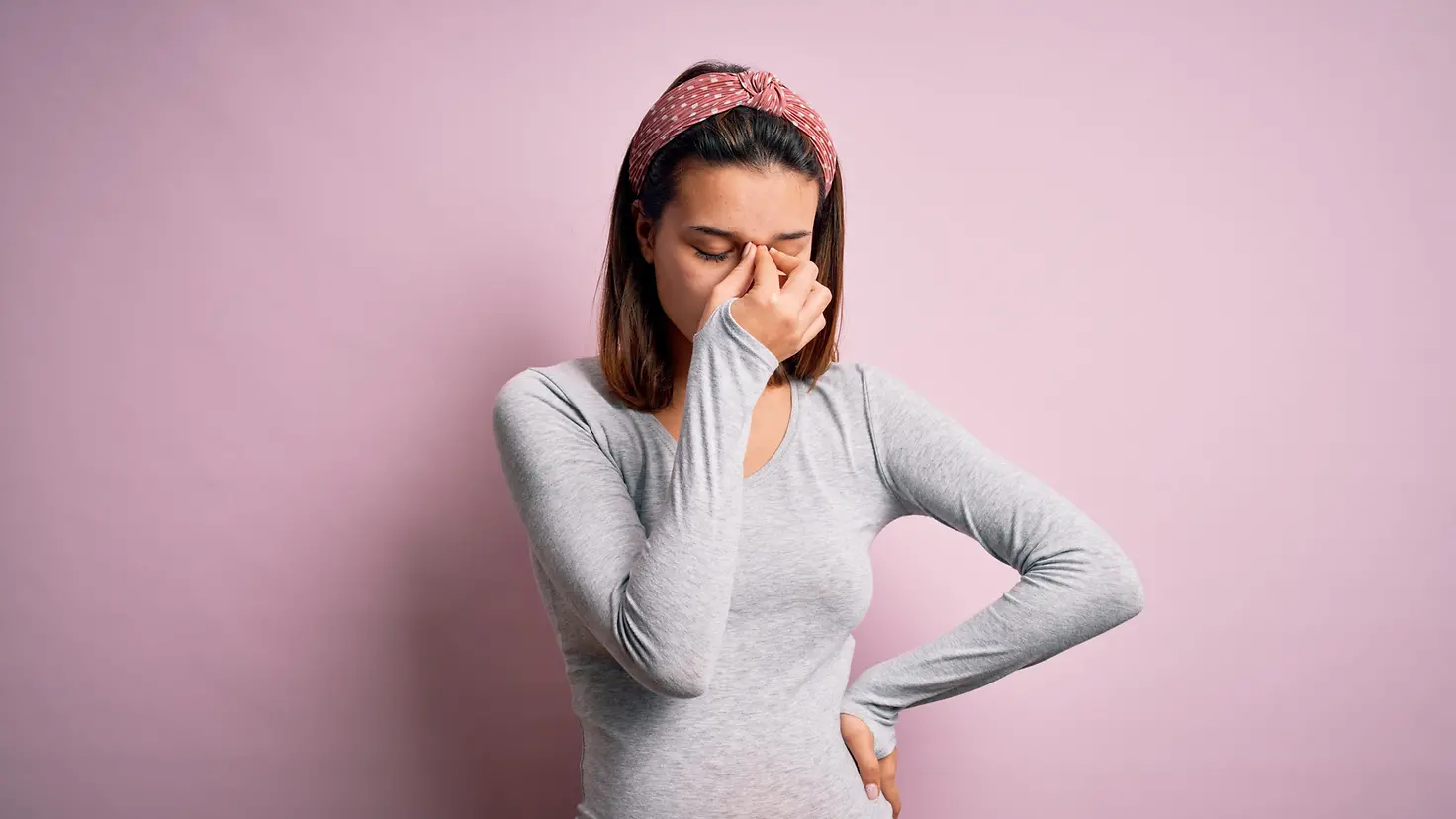 Das Bild zeigt eine schwangere Frau vor einer rosafarbenen Wand.