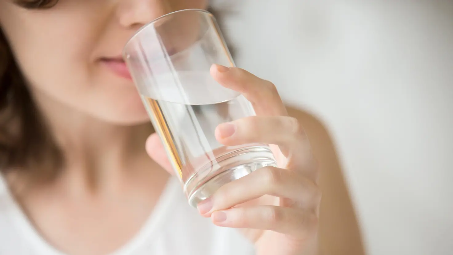Das Bild zeigt eine Frau, die Wasser aus einem Glas trinkt.
