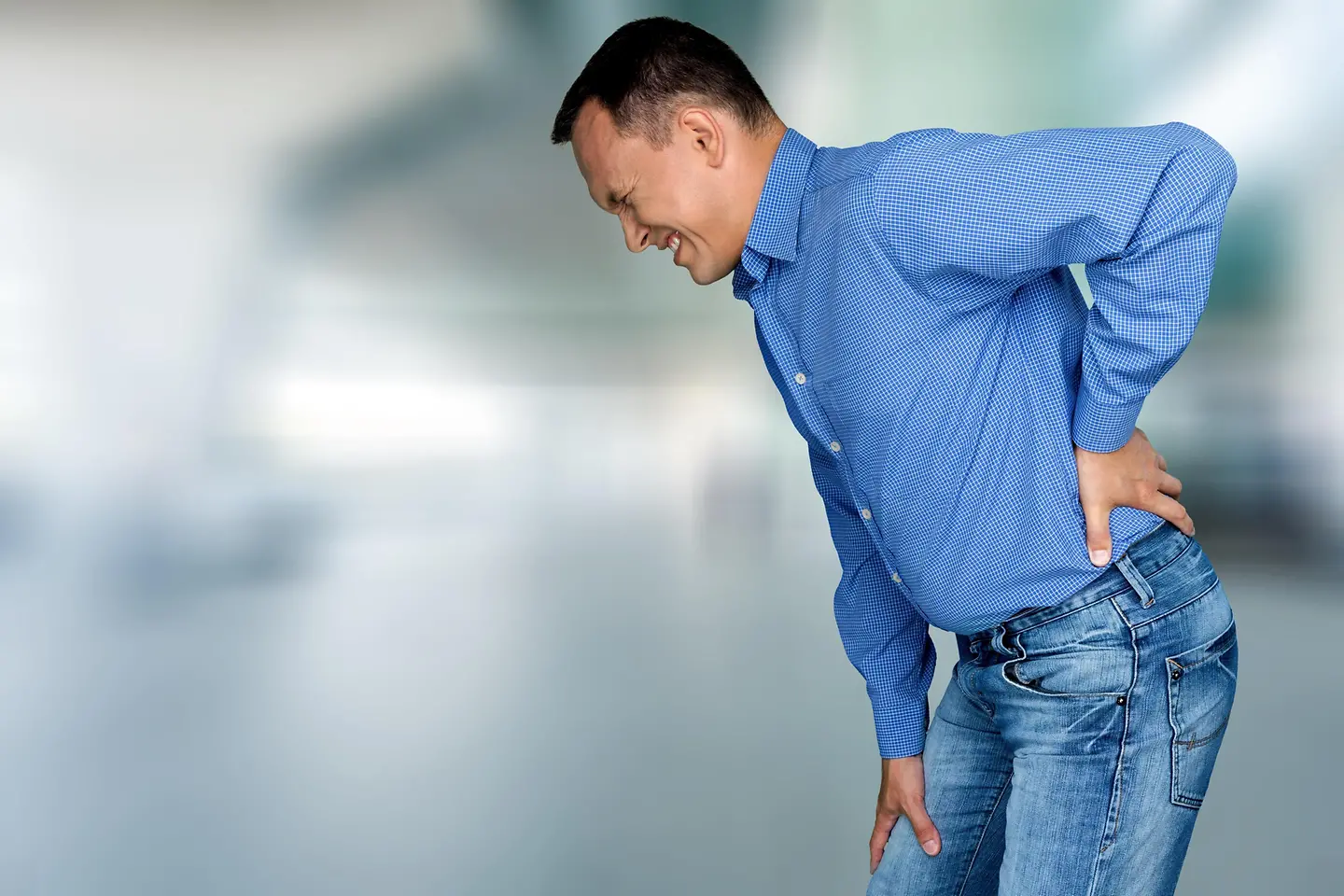 Das Bild zeigt einen Mann mit Hexenschuss, der sich mit schmerzverzerrtem Gesicht an den Rücken fasst.