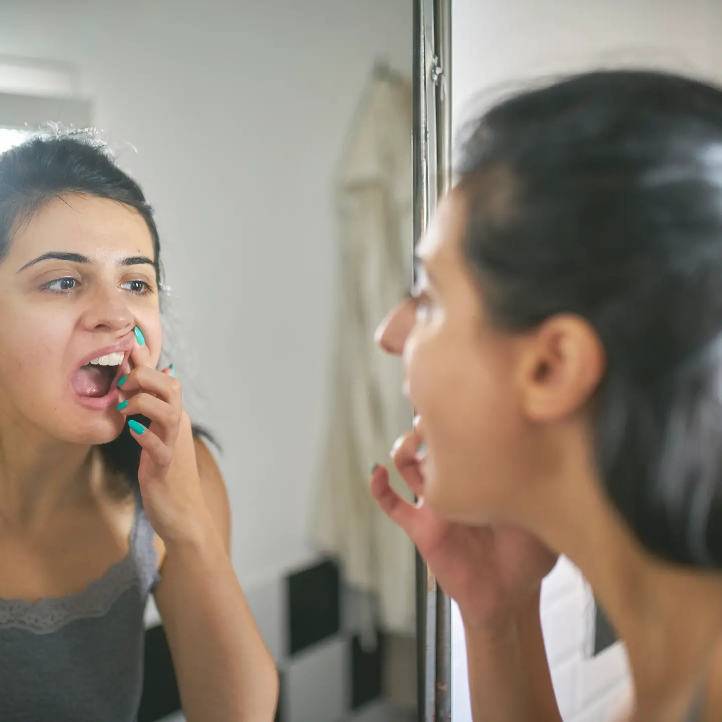 Eine junge Frau steht vor dem Spiegel und begutachtet kritisch ihre Zähne.