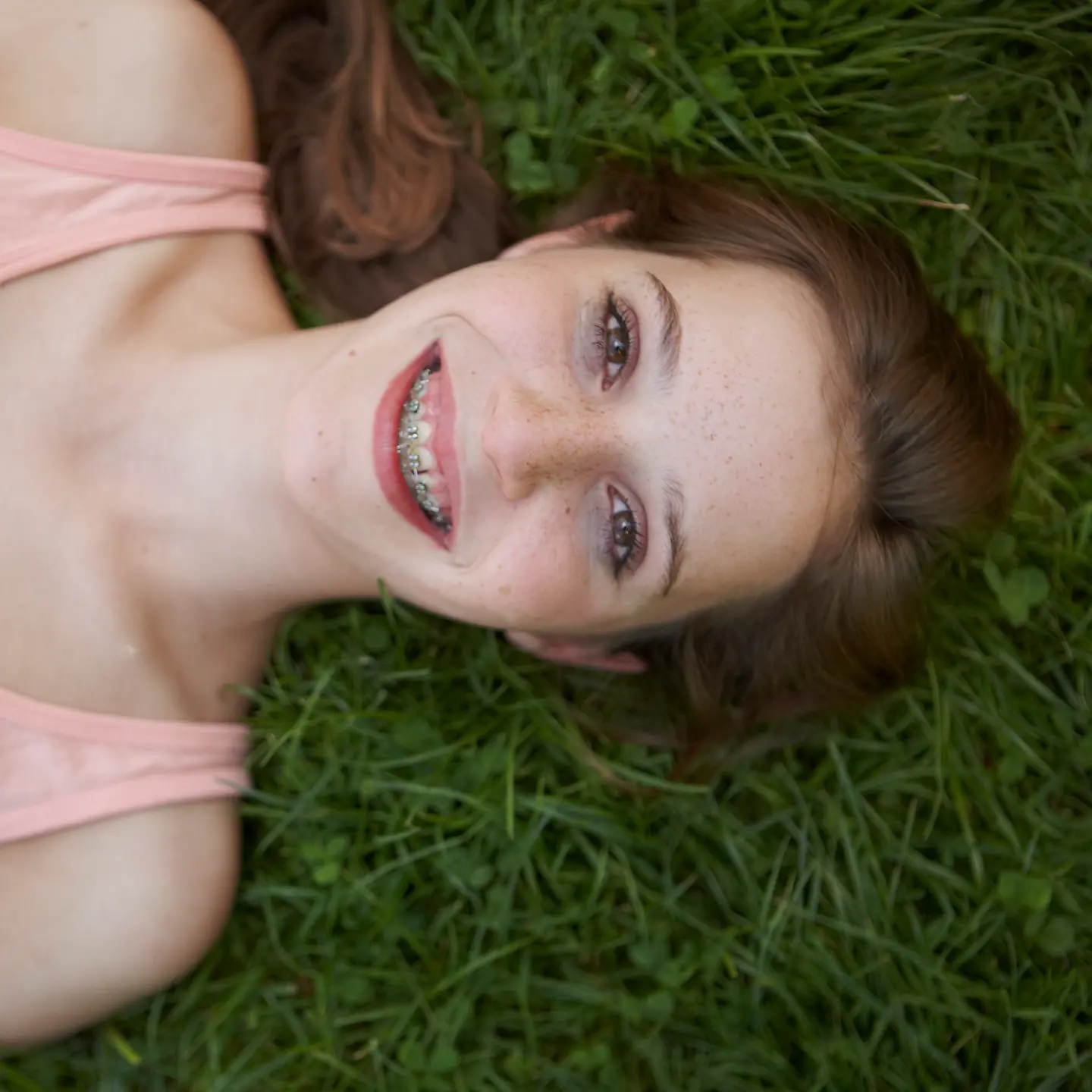 Mädchen mit fester Zahnspange liegt lachend im Gras.