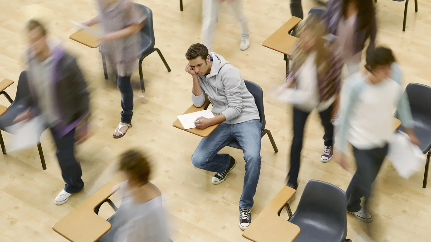 Student sitzt niedergeschlagen umgeben von wuselnden Studenten im Hörsaal