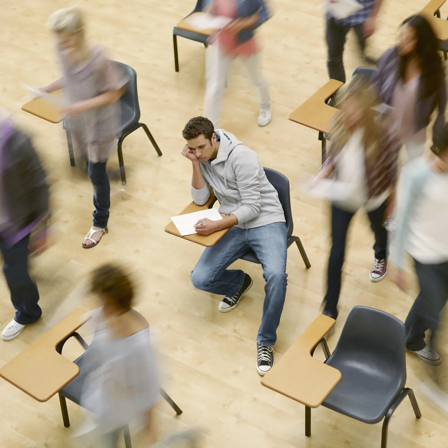 Student sitzt niedergeschlagen umgeben von wuselnden Studenten im Hörsaal