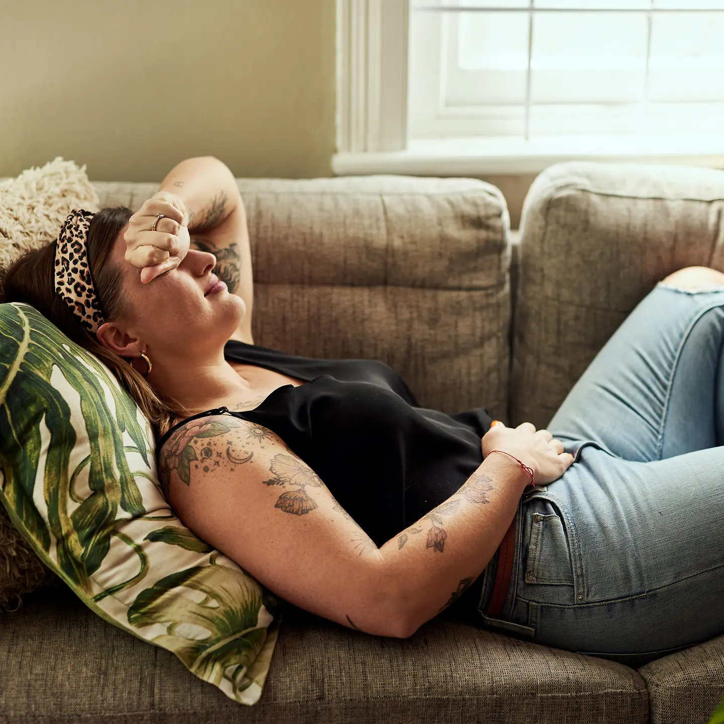 Eine junge Frau liegt mit Bauchschmerzen auf dem Sofa.