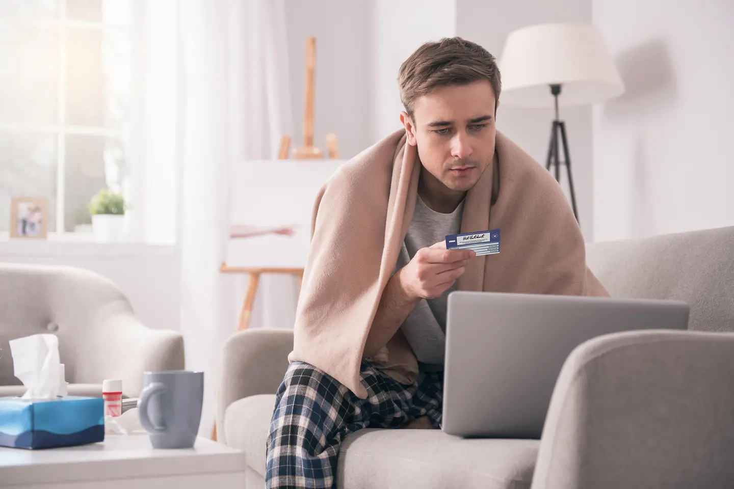 Kranker Mann vor dem Rechner, der seine Kreditkarte hält