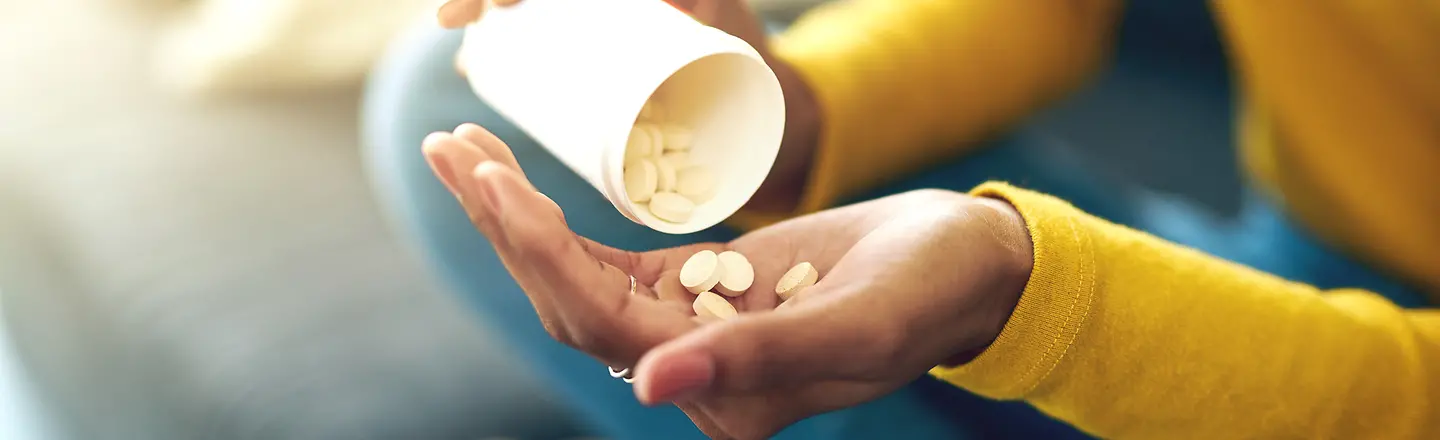 Eine Frau schüttet aus einem Behälter einige Tabletten in ihre linke Hand.