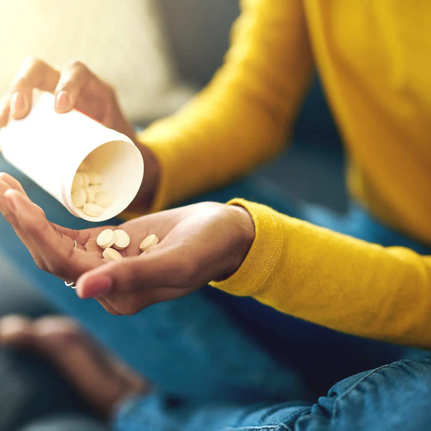 Eine Frau schüttet aus einem Behälter einige Tabletten in ihre linke Hand.