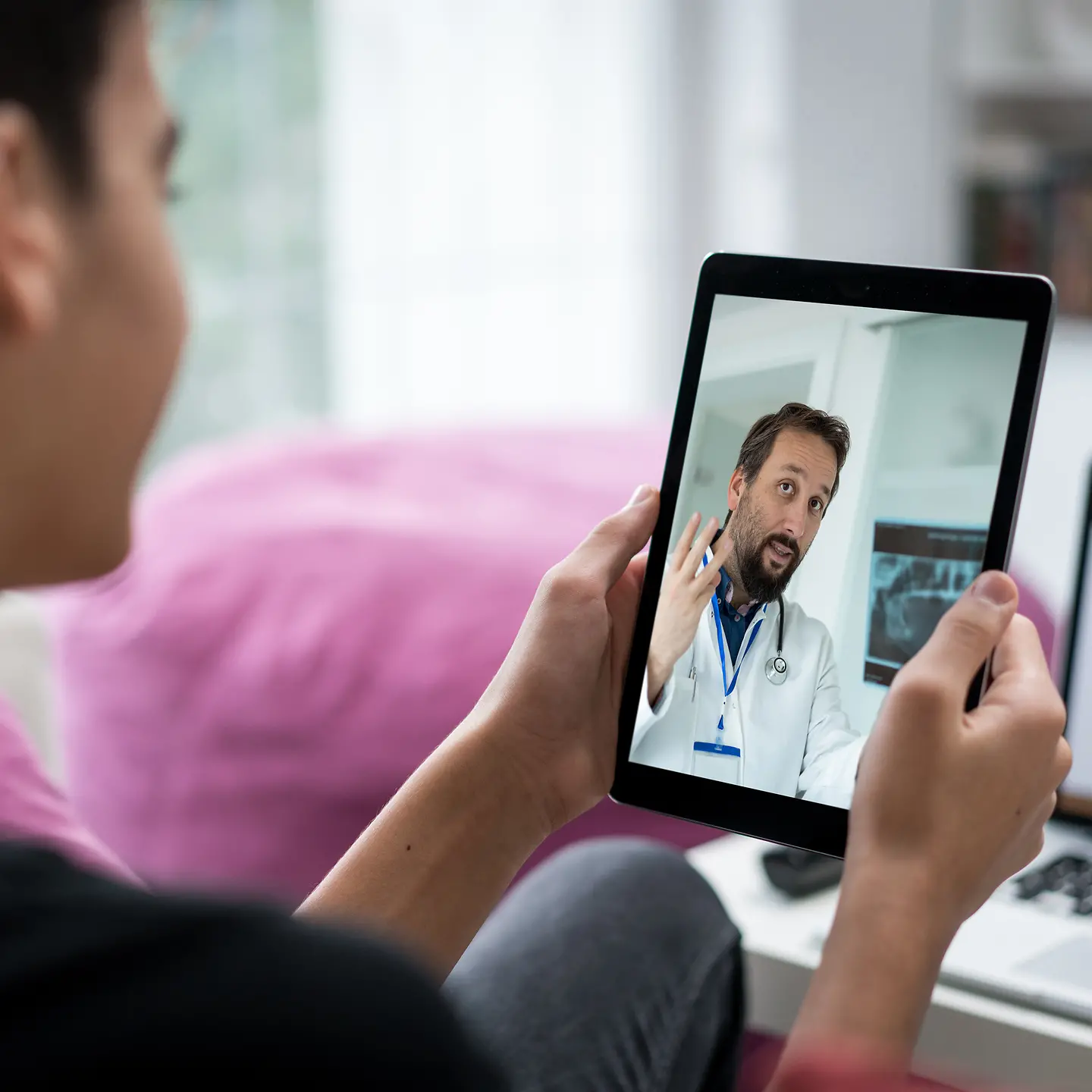 Ein Frau hält ein Tablet in der Hand, auf dem ein Arzt zu sehen ist.