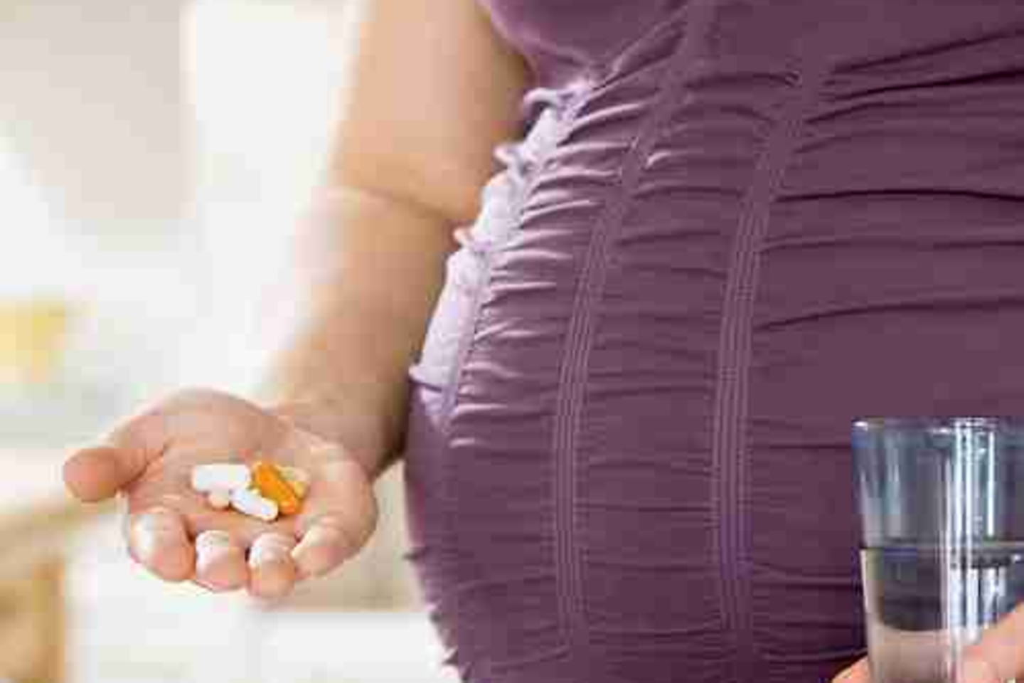 Eine schwangere Frau hält Tabletten und ein Glas Wasser in der Hand. 