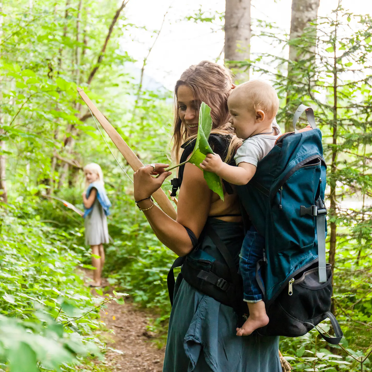 Eine junge Mutter wandert mit ihrem Sohn auf dem Rücken durch den Wald.