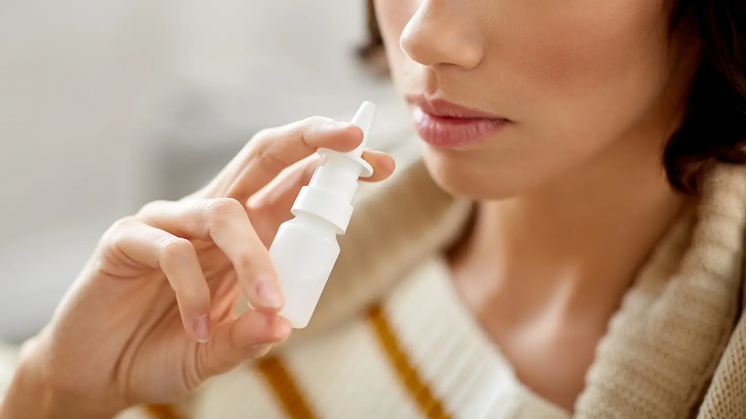 Das Bild zeigt eine Frau, die Nasenspray verwendet.