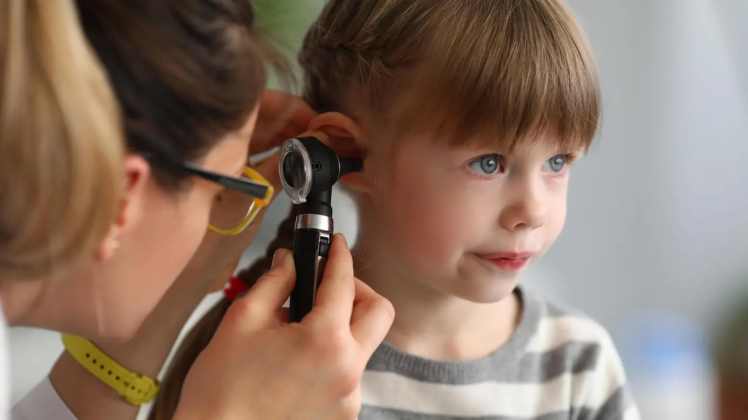 Das Bild zeigt ein Mädchen, deren Ohr von einer Ärztin untersucht wird.