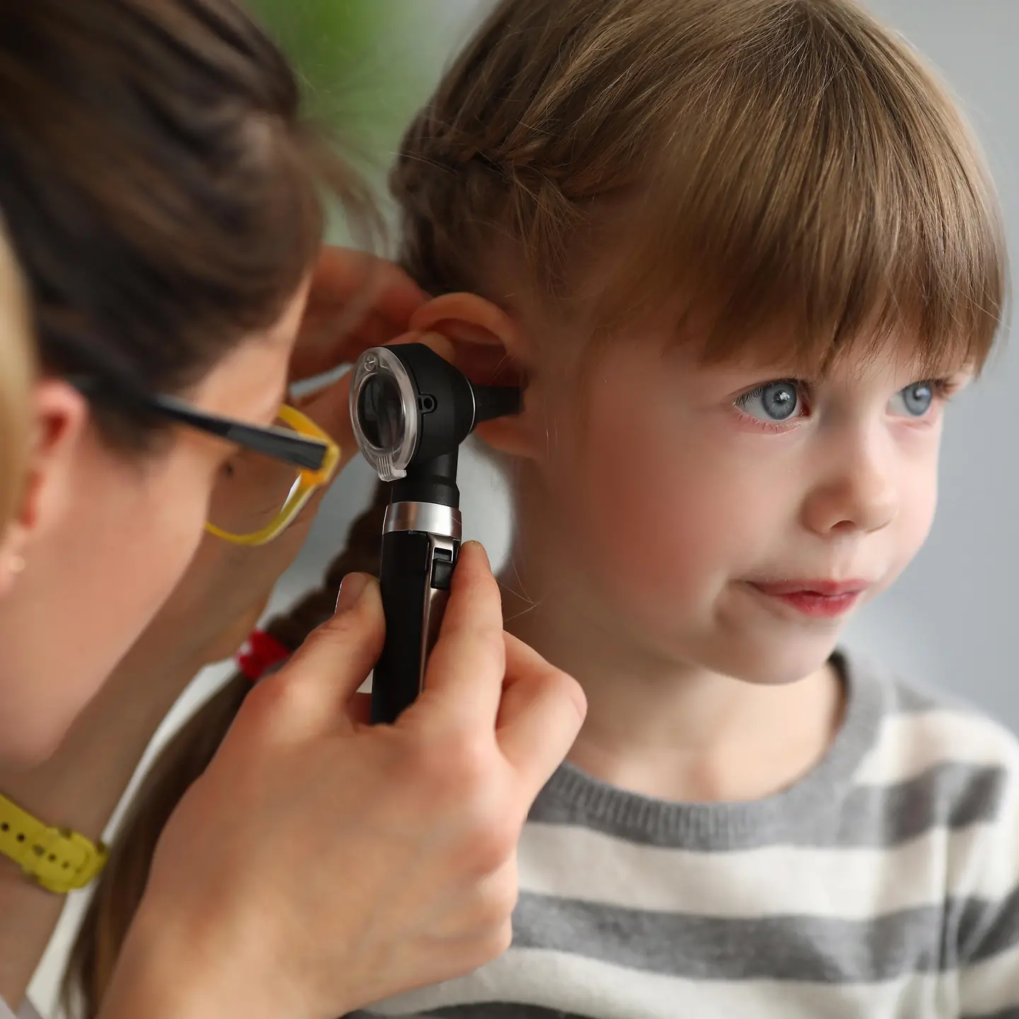 Das Bild zeigt ein Mädchen, deren Ohr von einer Ärztin untersucht wird.