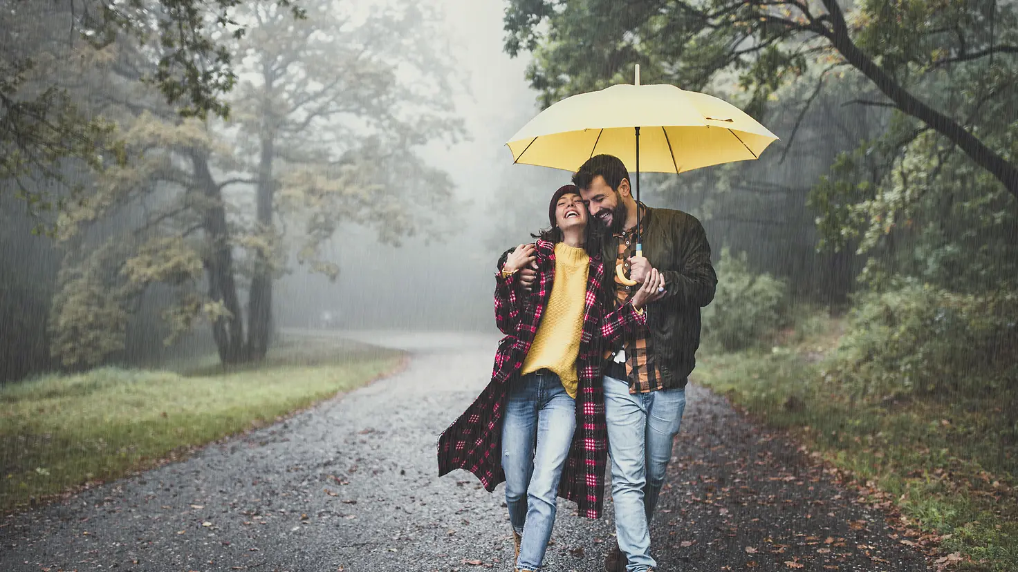 Ein Paar geht mit einem Regenschirm durch eine Allee