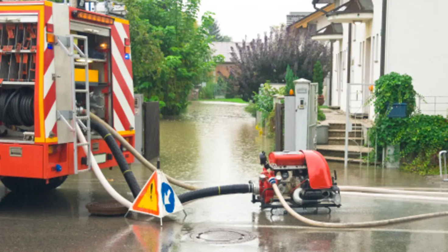 Ein Feuerwehrfahrzeug steht auf einer Straße und pumpt Wasser aus einem überfluteten Haus.