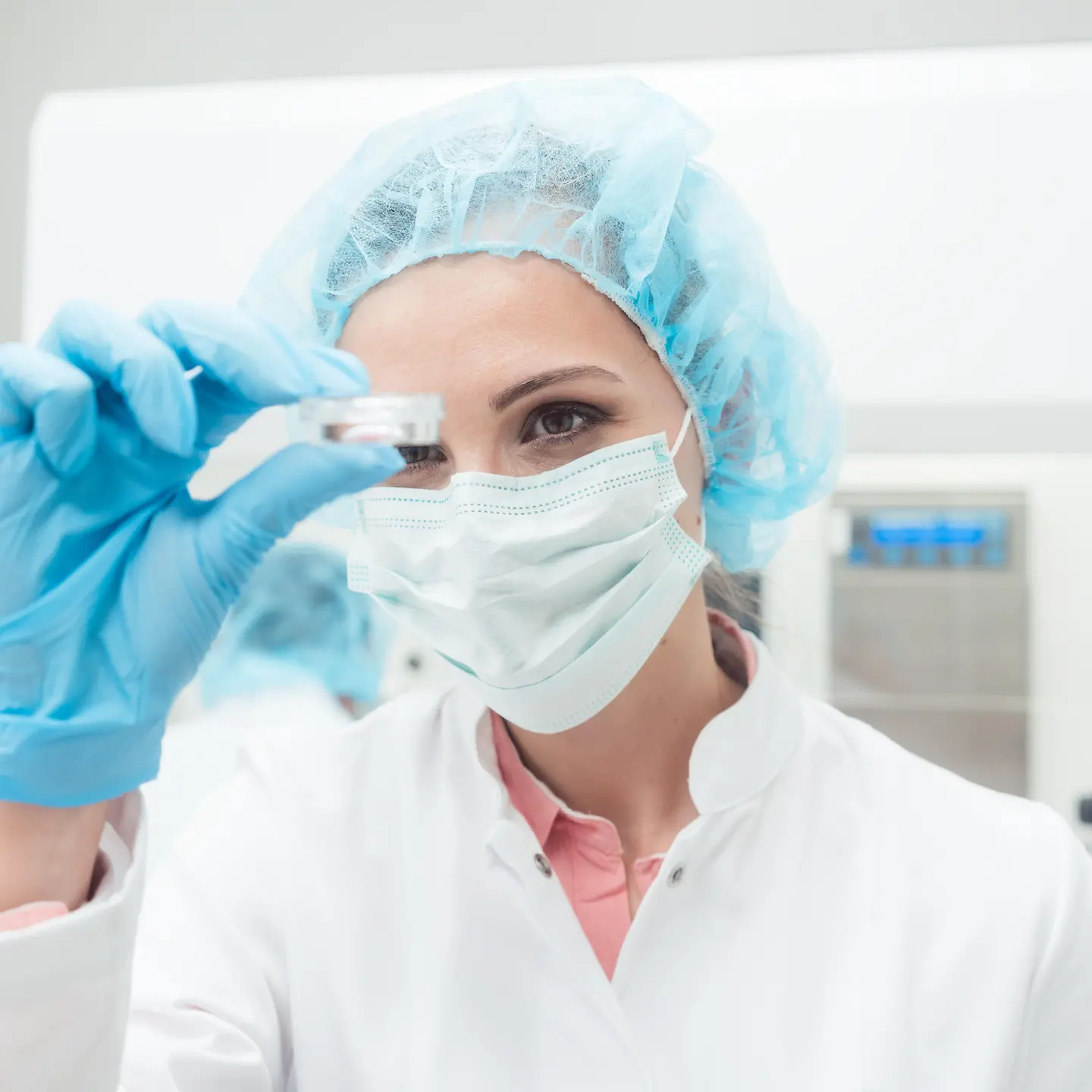 Eine Frau mit Laborkittel und Haarschutz hält eine Petrischale in der Hand