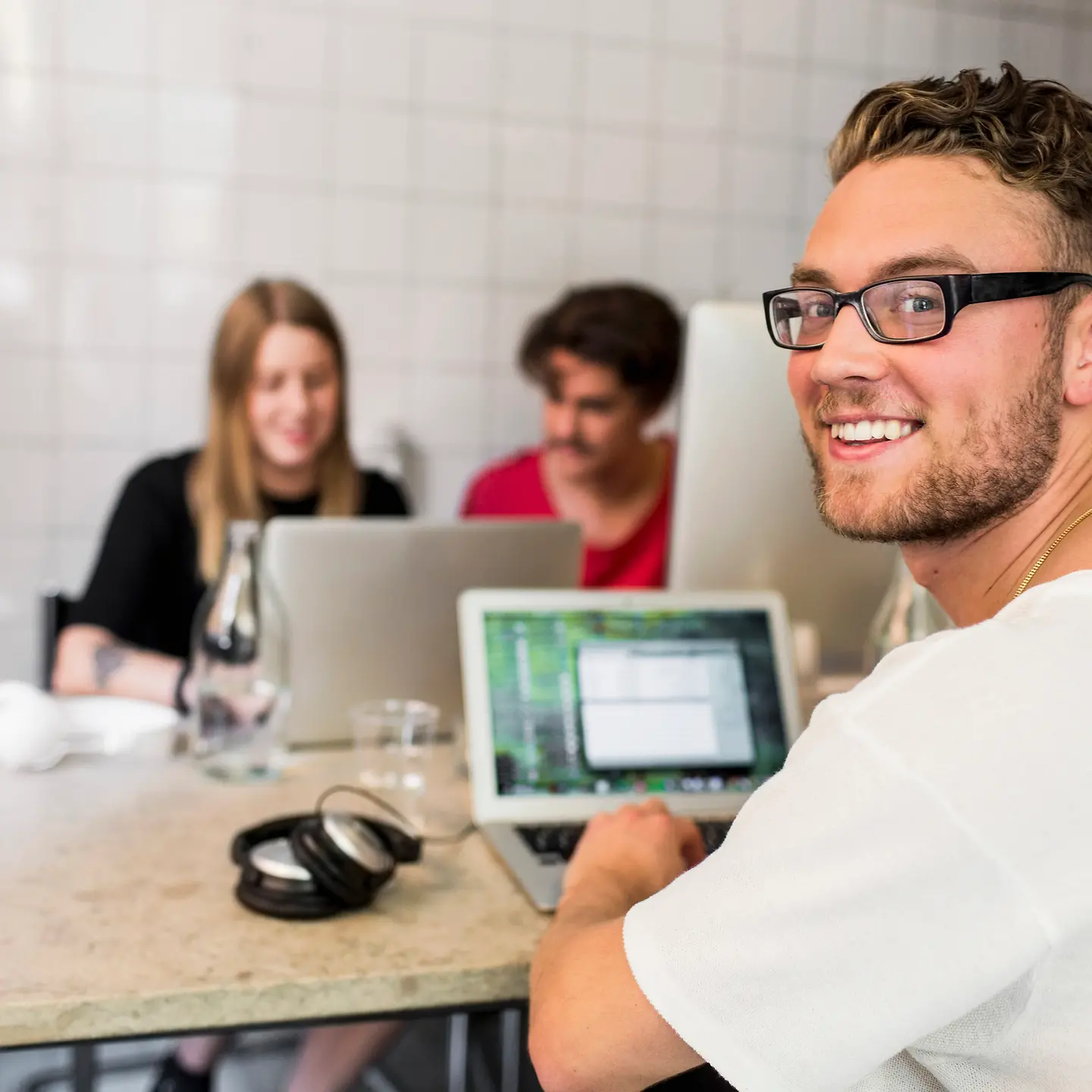 Ein junger Mann sitzt in einem Büro am Schreibtisch und schaut in die Kamera.