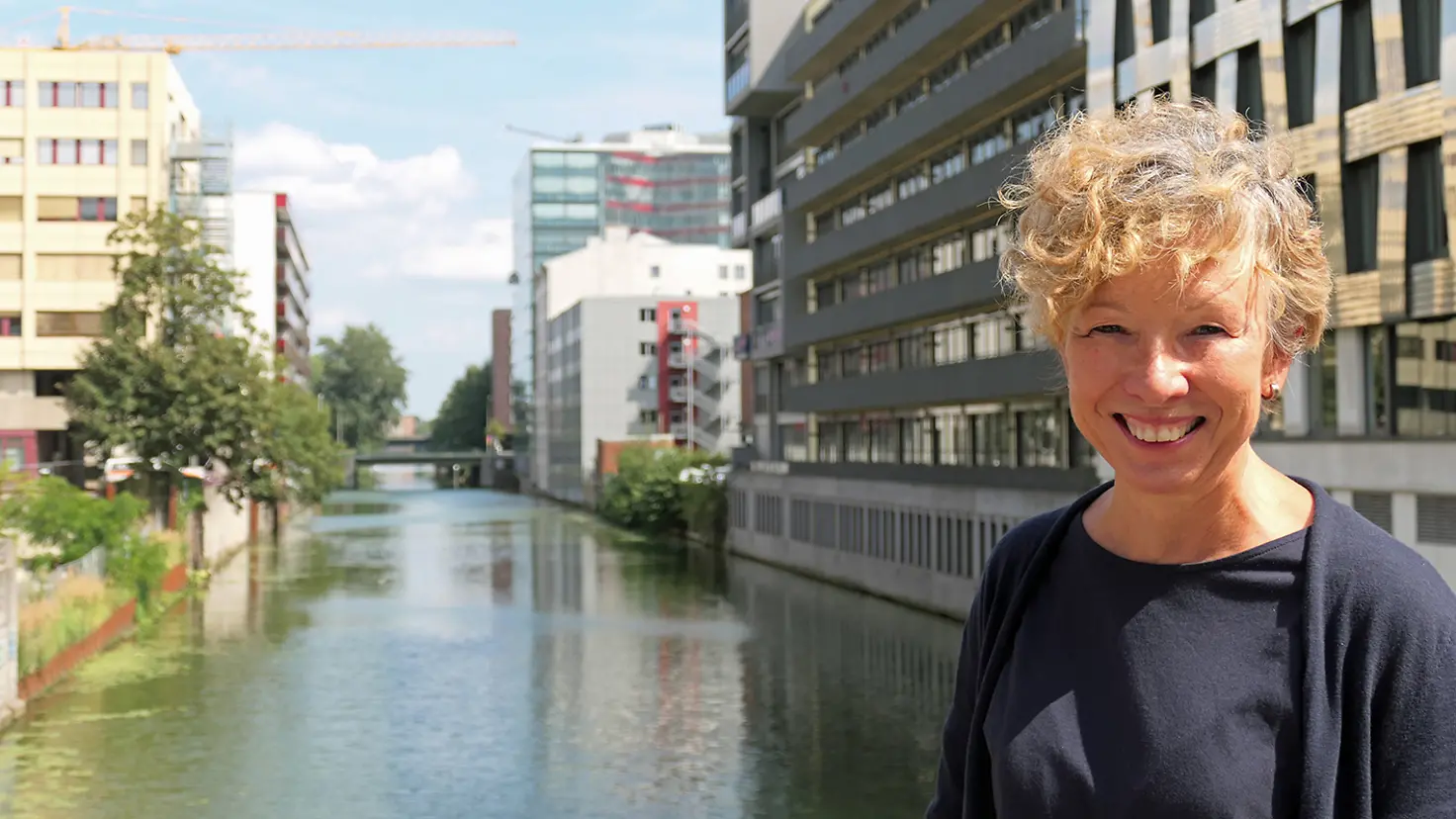 eine lächelnde Frau mit blonden lockigen Haaren steht auf einer Brücke über einen Kanal im Stadtteil Hamburg Hammerbrook