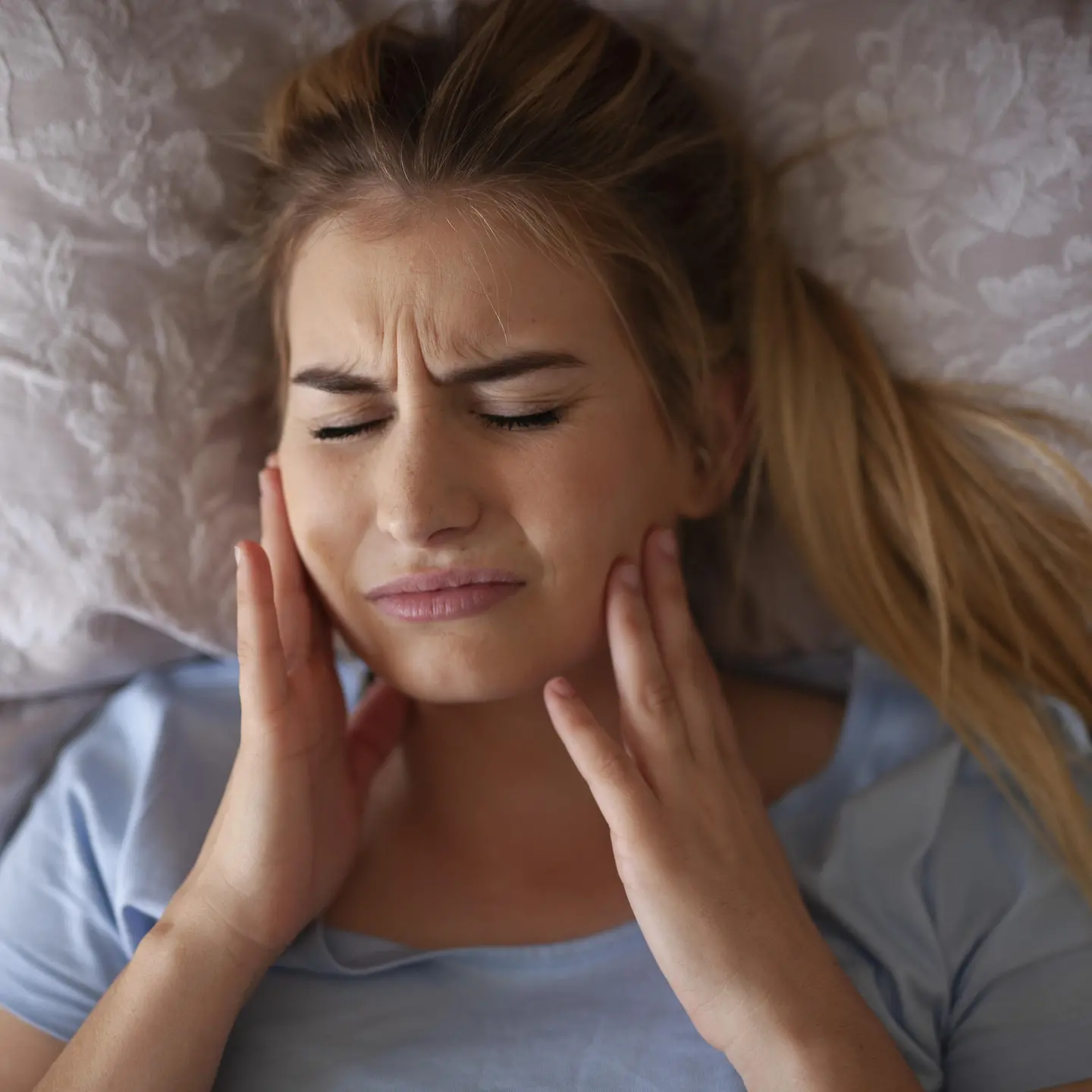 Das Bild zeigt eine Frau, die mit Kieferschmerzen im Bett liegt.