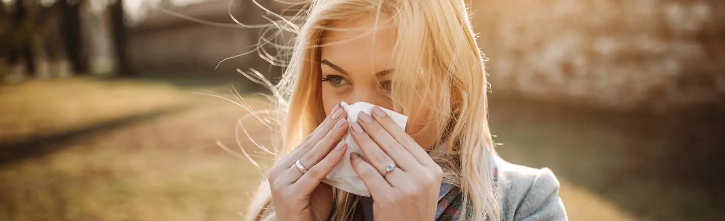 Eine junge Frau putzt sich mit einem Taschentuch die Nase.