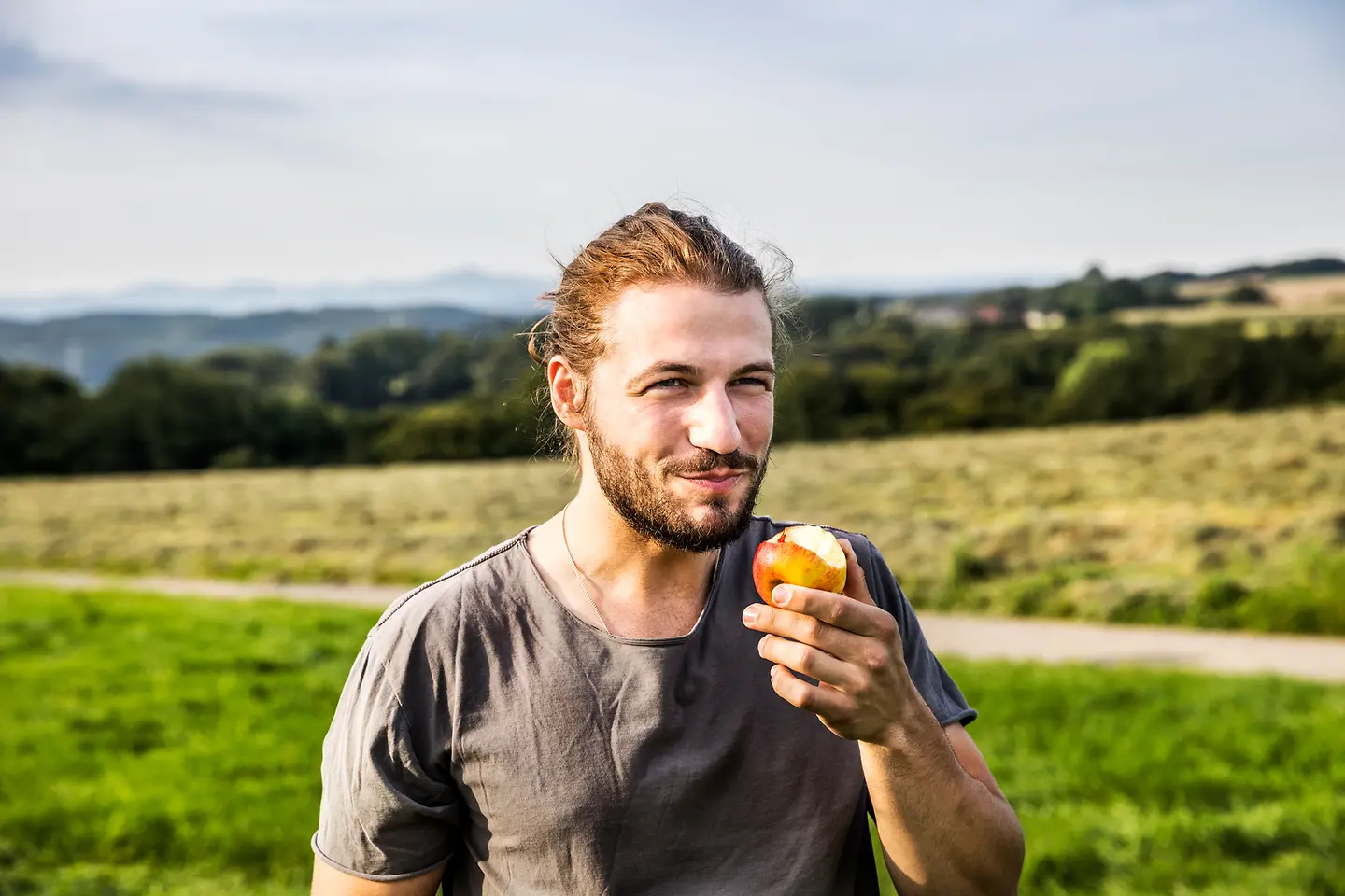 Porträt eines jungen Mannes, der draußen mit einem angebissenen Apfel steht