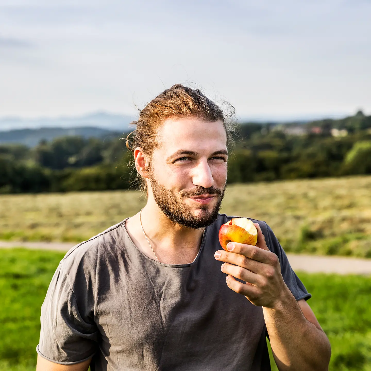 Porträt eines jungen Mannes, der draußen mit einem angebissenen Apfel steht