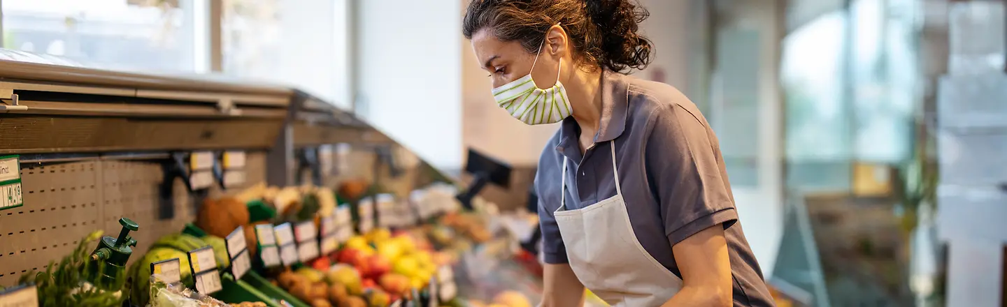 Weibliche Mitarbeiterin arrangiert frisches Obst und Gemüse in der Abteilung für Lebensmittel im Supermarkt.