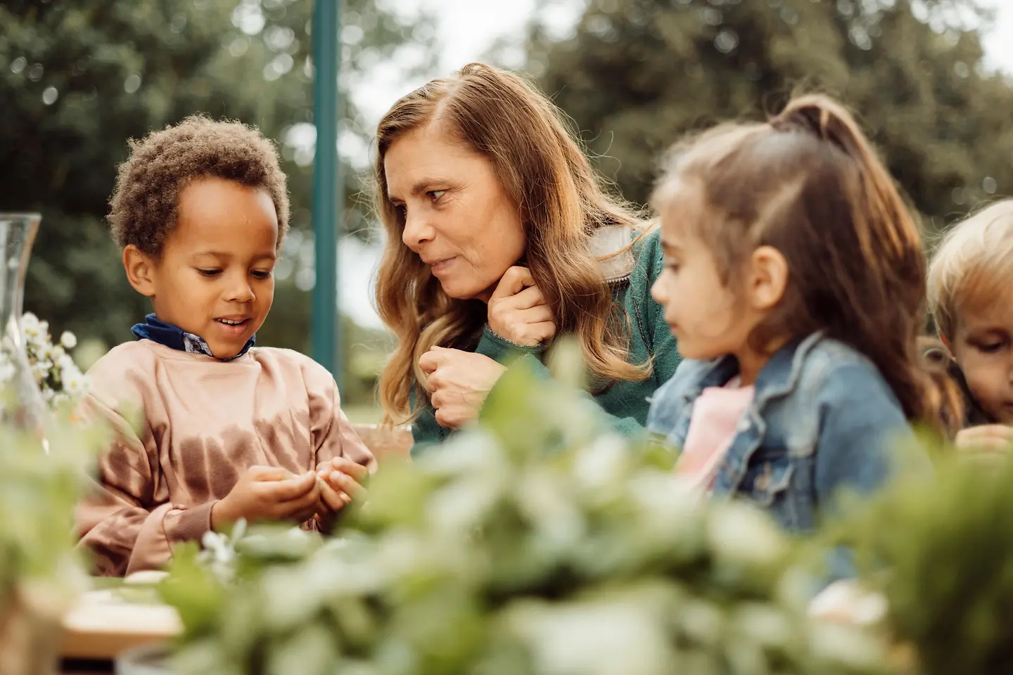 Sarah Wiener sitzt mit drei Kindern draußen an einem Tisch auf dem Gemüse liegt