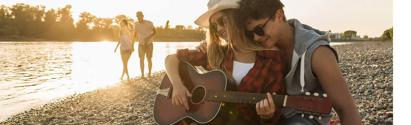 Zwei Jugendliche mit Gitarre entspannt am Flussufer