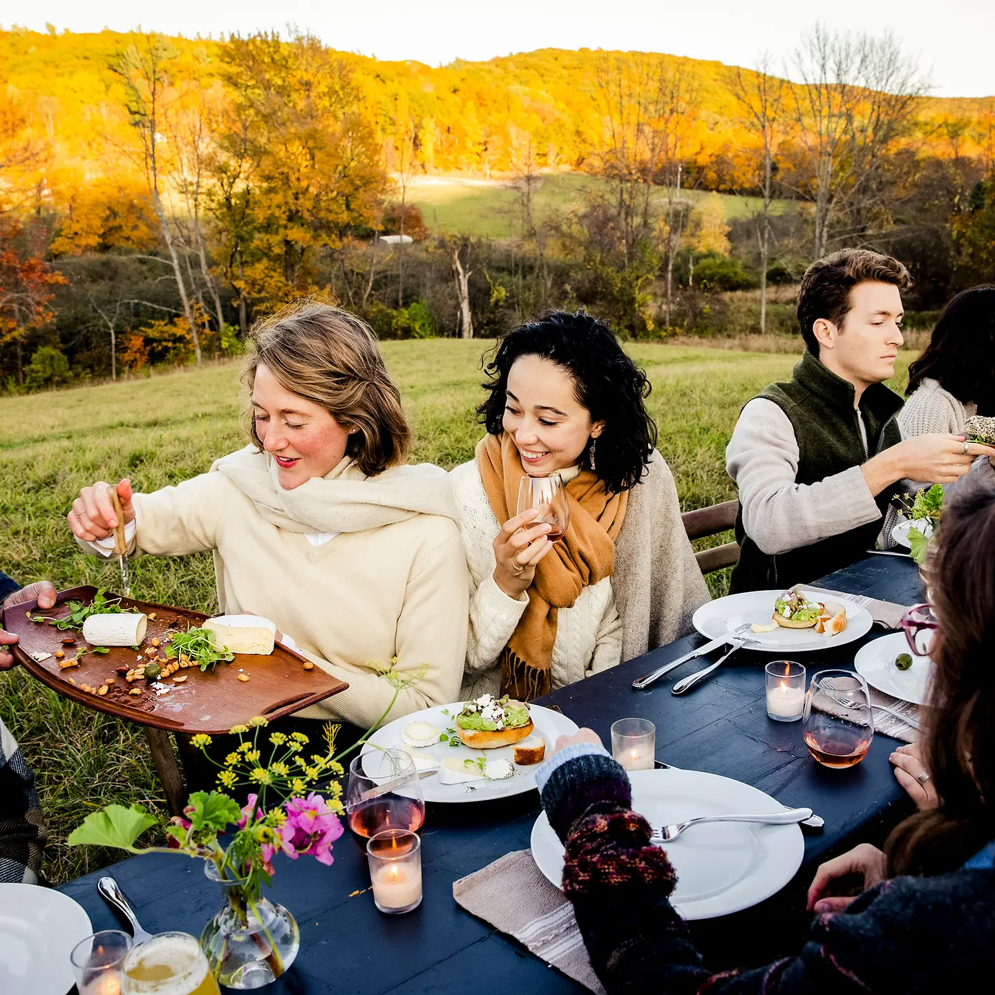 Eine Gruppe Menschen isst gemeinsam draußen im Herbst an einer langen Tafel