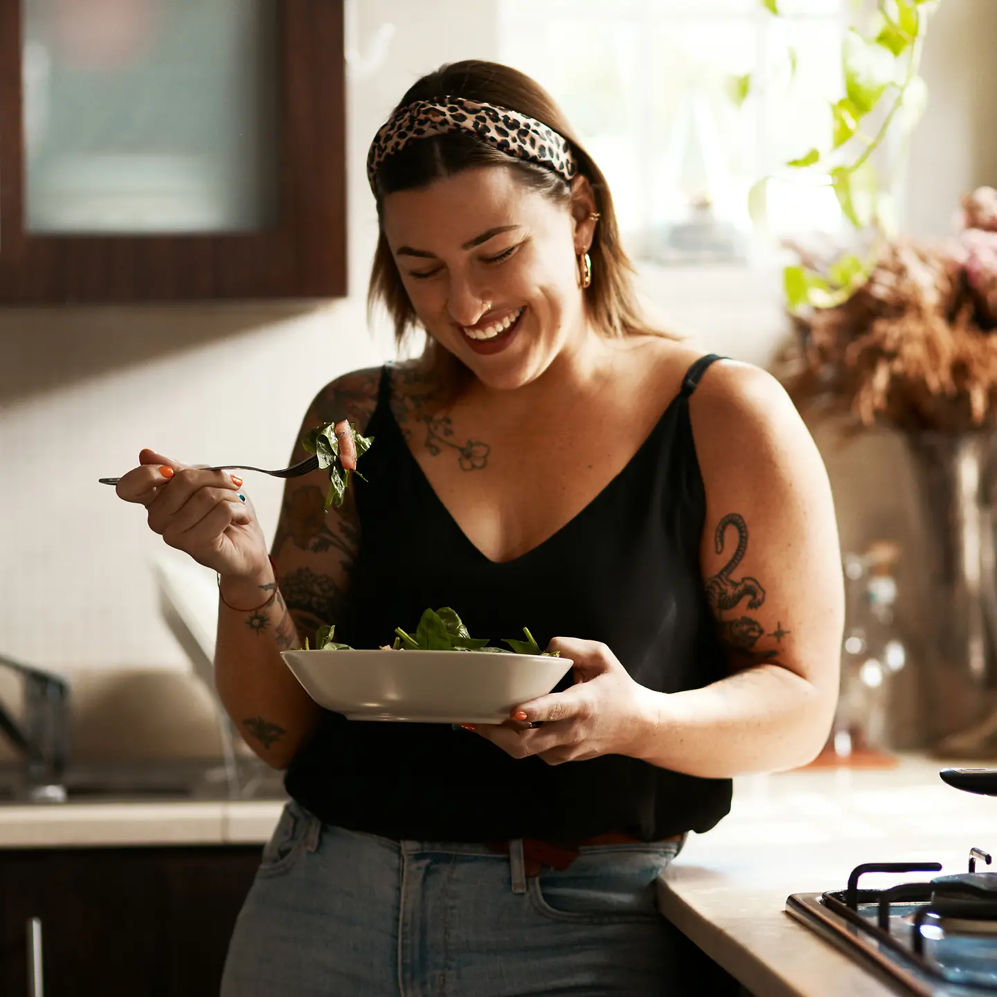 Eine junge Frau steht mit Salatschüssel am Fenster und lacht