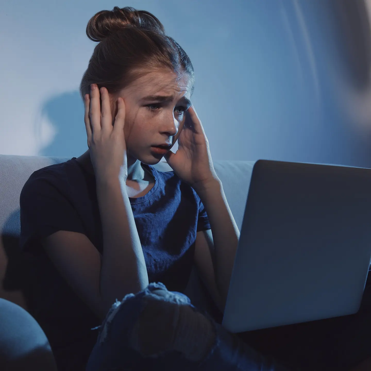 Ein Mädchen sitzt vor dem Laptop und fasst sich an die Schläfen.