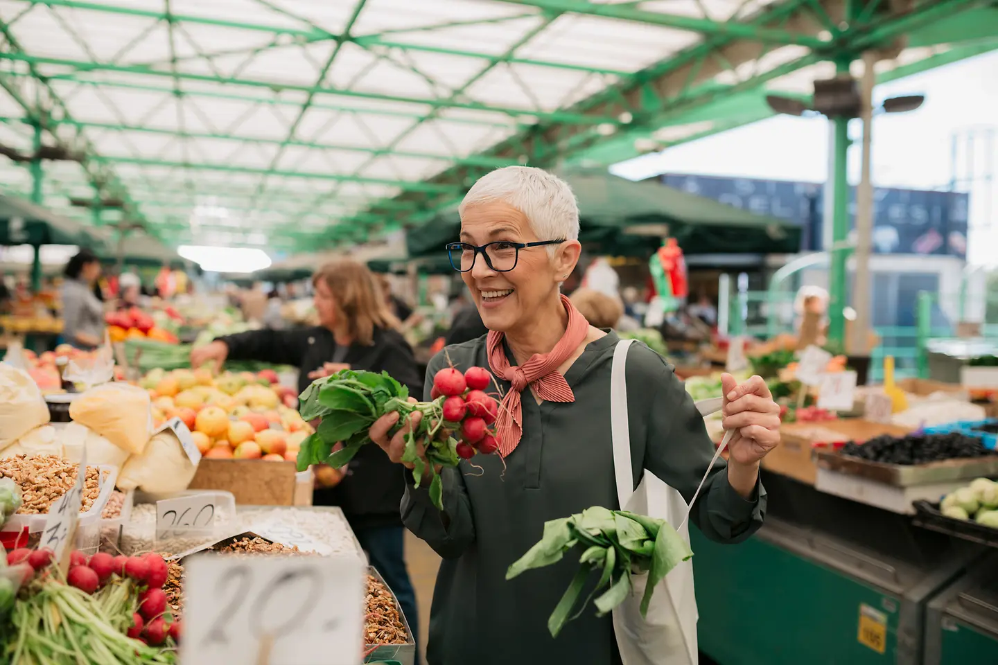 Lächelnde ältere Frau mit kurzen grauen Haaren kauft Lebensmittel auf dem Wochenmarkt ein