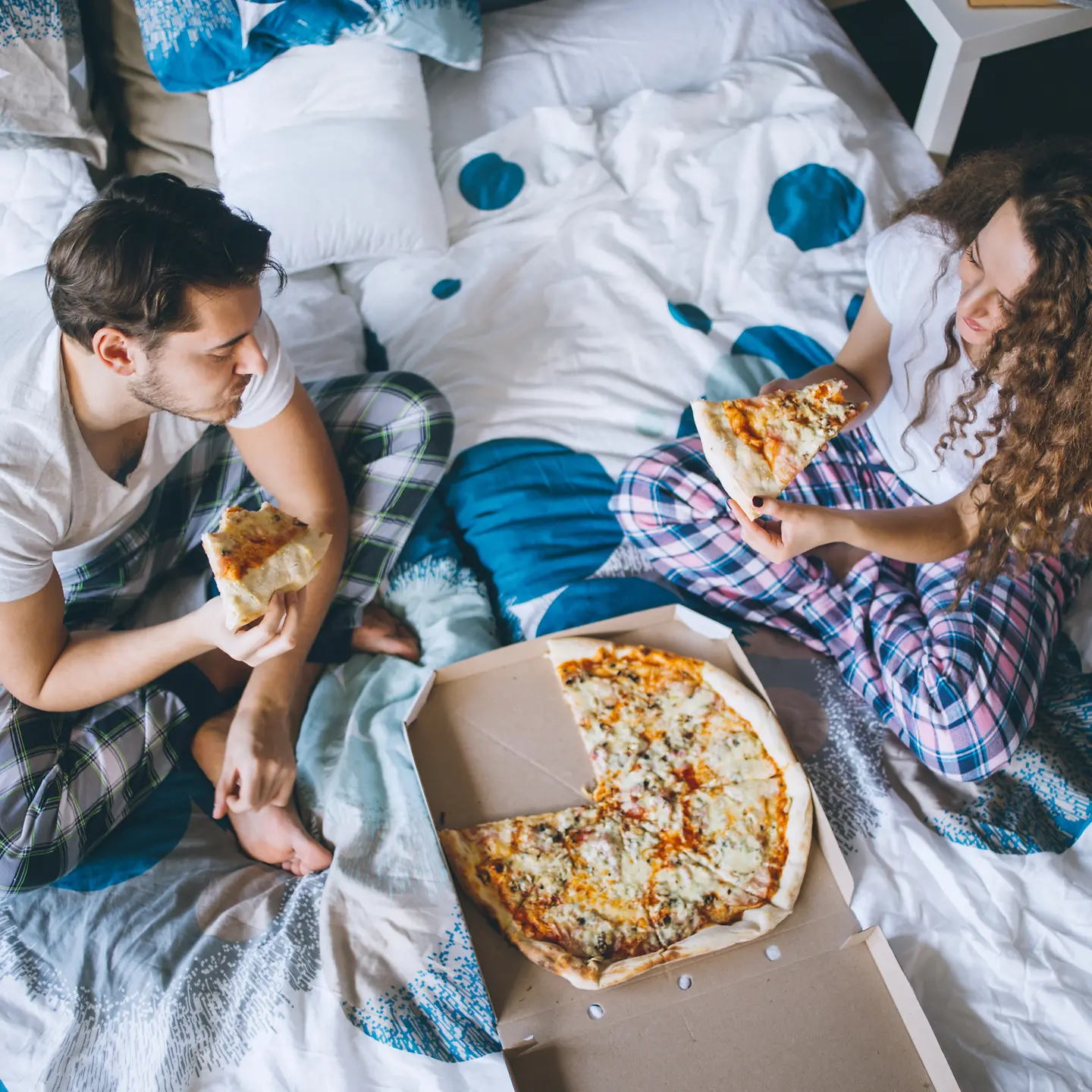 Ein junges Paar isst gemeinsam im Bett Pizza.
