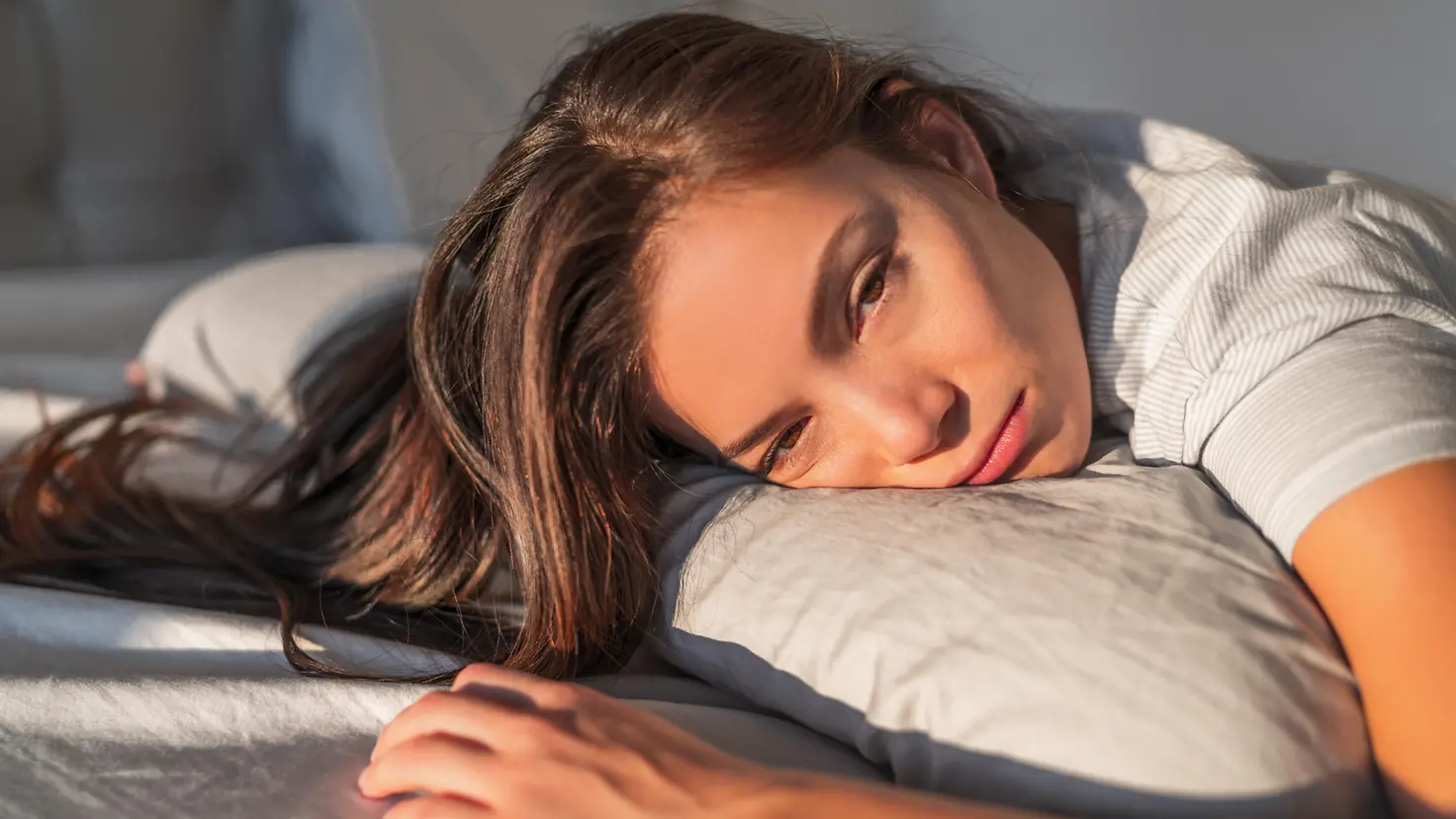 Das Bild zeigt eine Frau, die müde auf dem Bett liegt.
