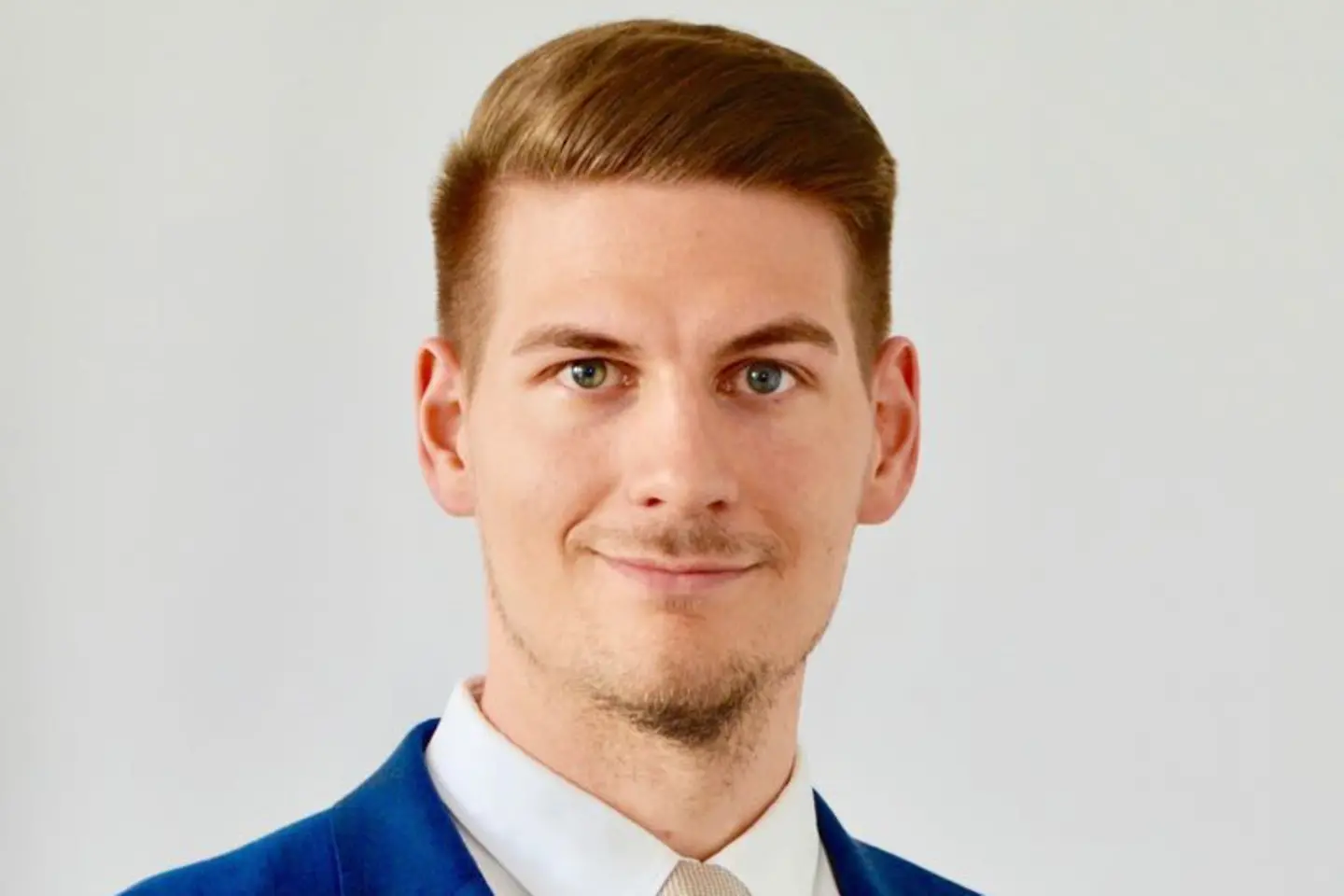 Ein junger Mann mit blauem Anzug und Krawatte lächelt in die Kamera