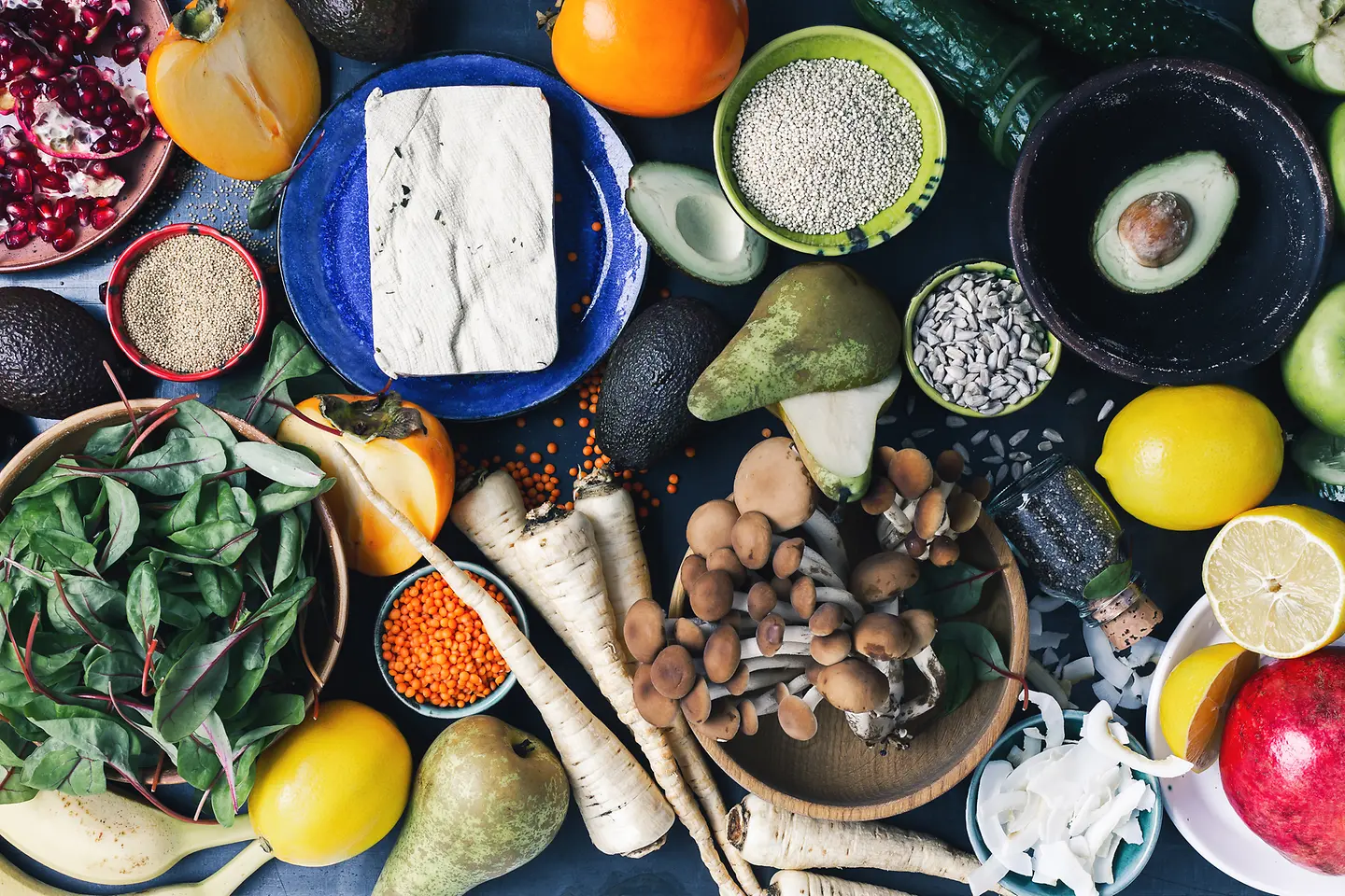 Draufsicht auf einen Tisch mit vielen pflanzlichen Lebensmitteln, frischem Obst, Gemüse, trockenen Körnern und Samen.