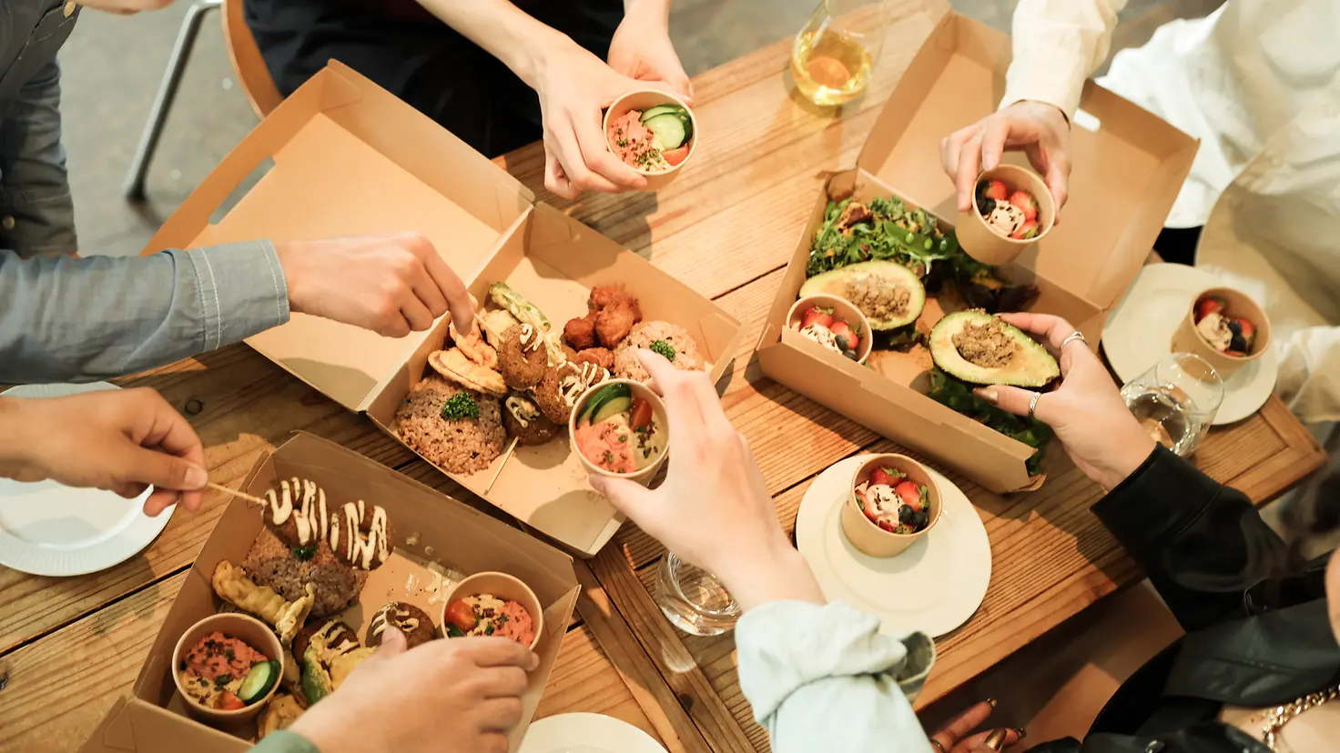 Draufsicht auf eine Gruppe von Menschen, die zusammen am Tisch veganes Essen mit plastikfreier Verpackung genießen.