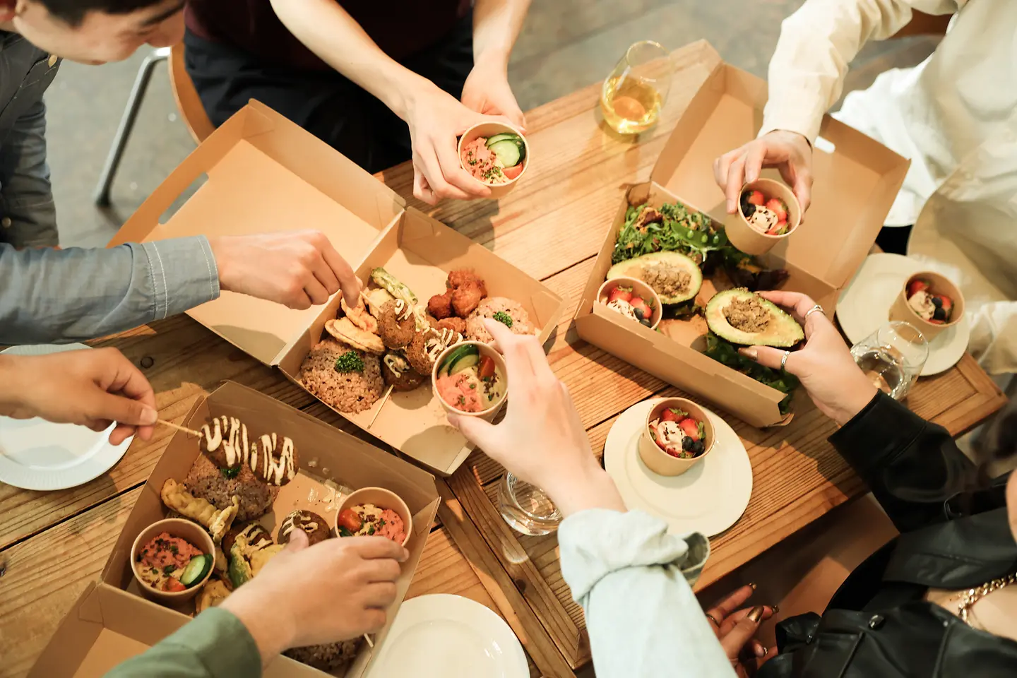 Draufsicht auf eine Gruppe von Menschen, die zusammen am Tisch veganes Essen mit plastikfreier Verpackung genießen.