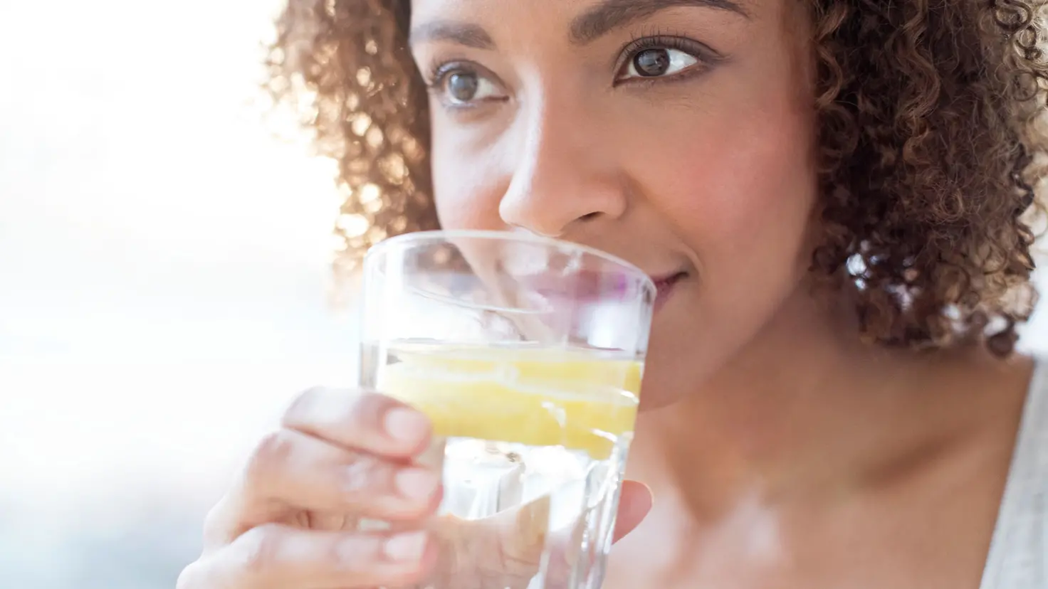 Eine junge Frau trinkt aus einem Glas Wasser mit einer Zitronenscheibe