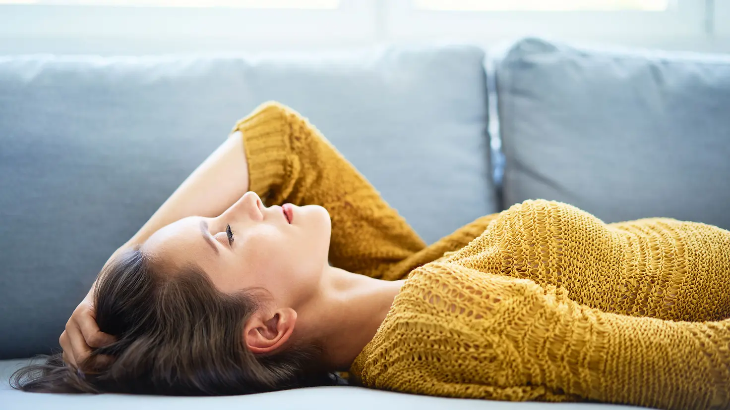 Junge Frau liegt mit geschlossenen Augen auf dem Sofa und entspannt sich