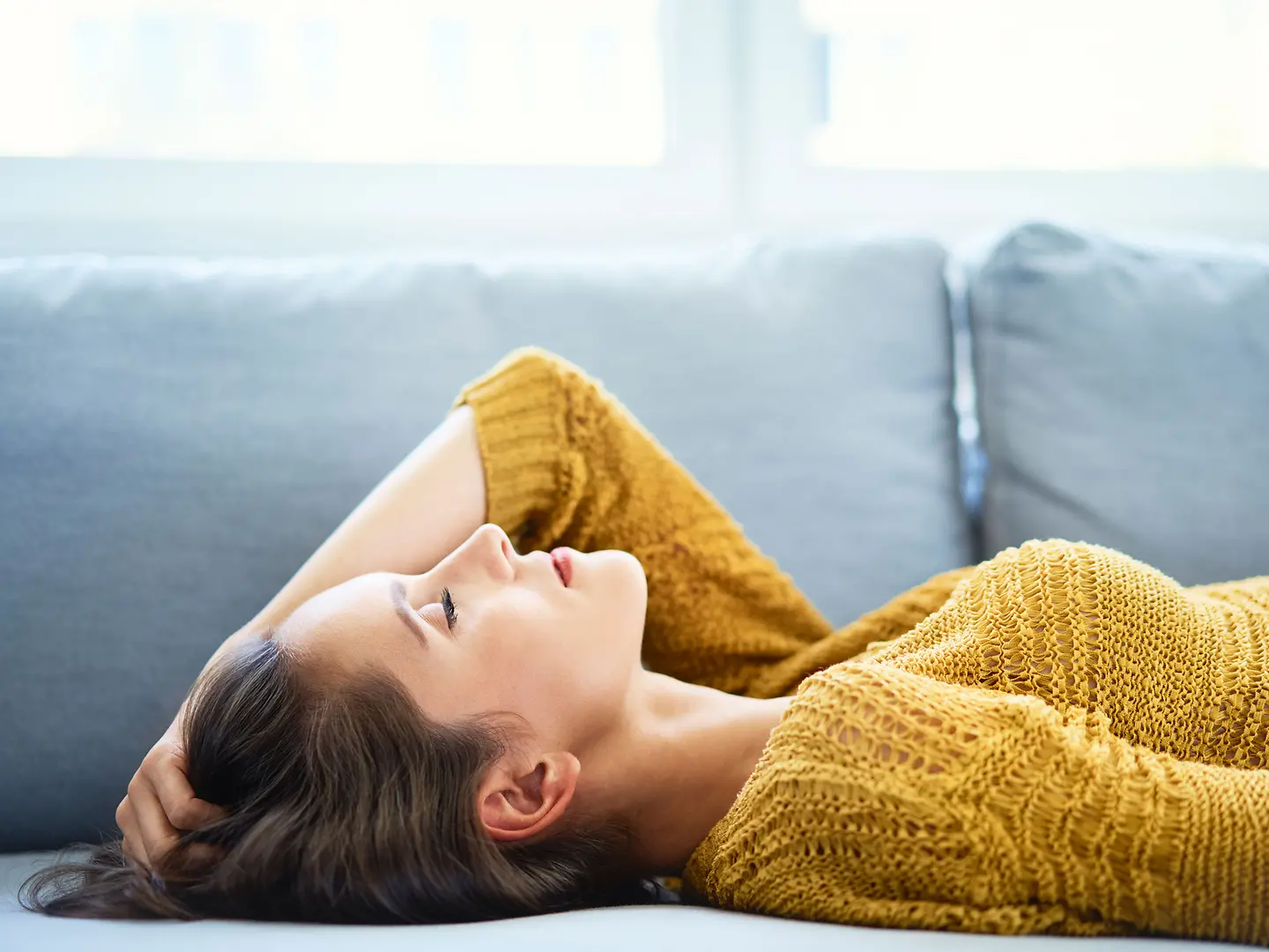 Junge Frau liegt mit geschlossenen Augen auf dem Sofa und entspannt sich