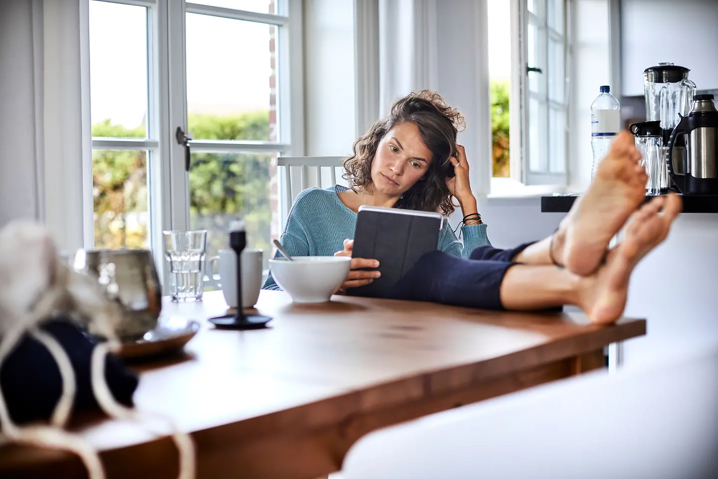 Eine junge Frau sitzt entspannt am Tisch und benutzt ein Tablet